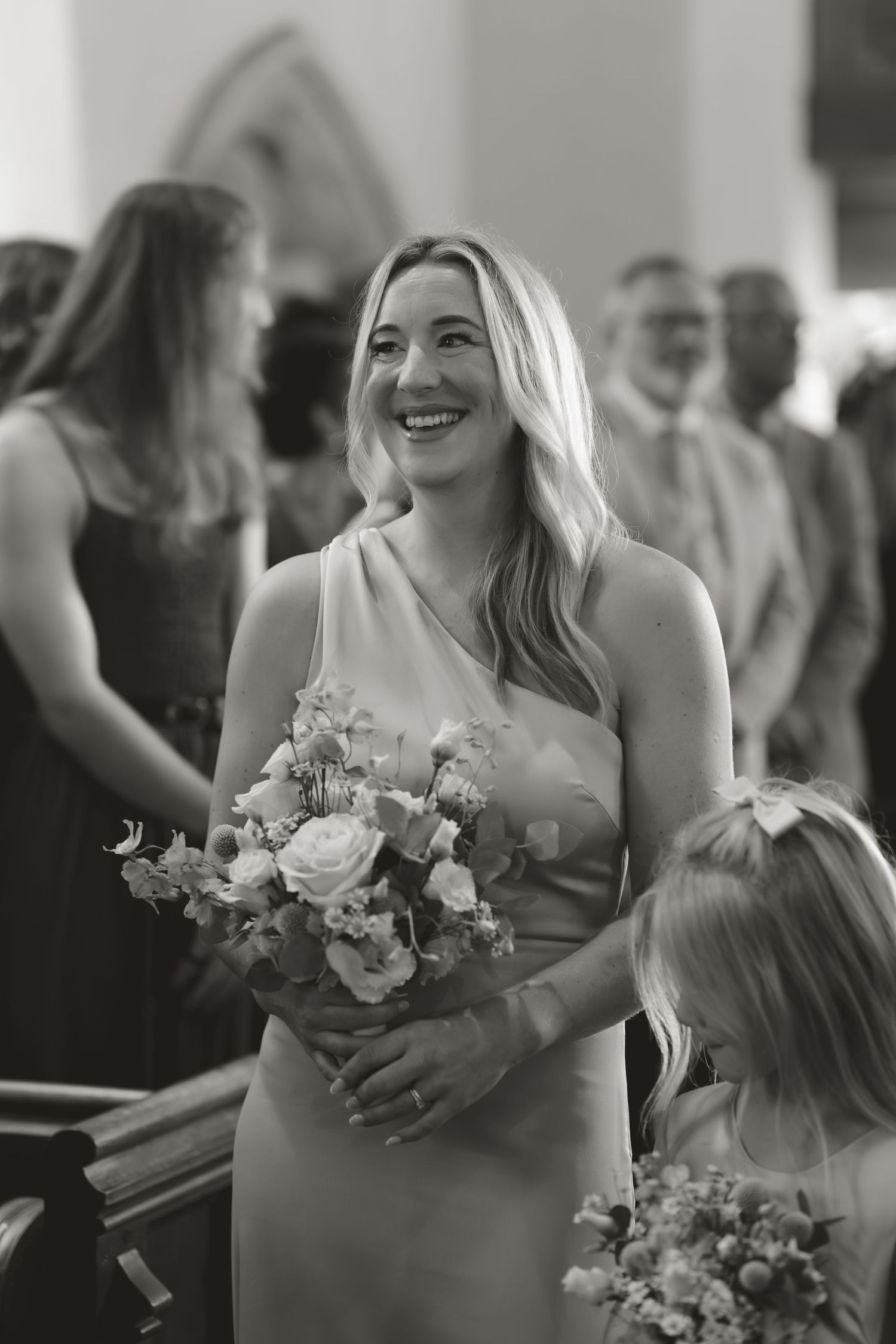 A bridesmaid in a blush dress holds a beautiful bouquet of roses and mixed flowers during a church ceremony.