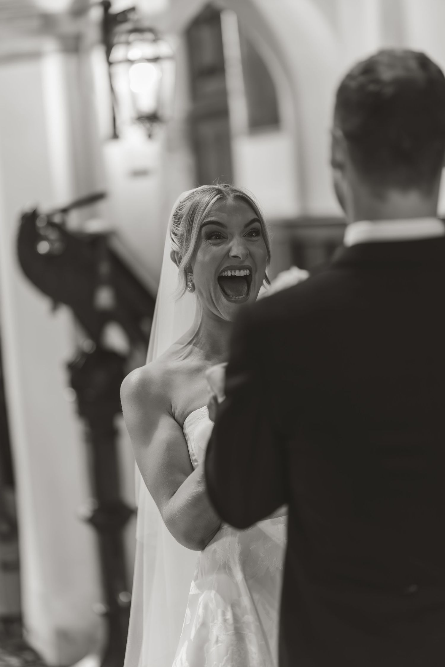 Black and white candid wedding photography capturing joyful expressions in an elegant indoor setting.