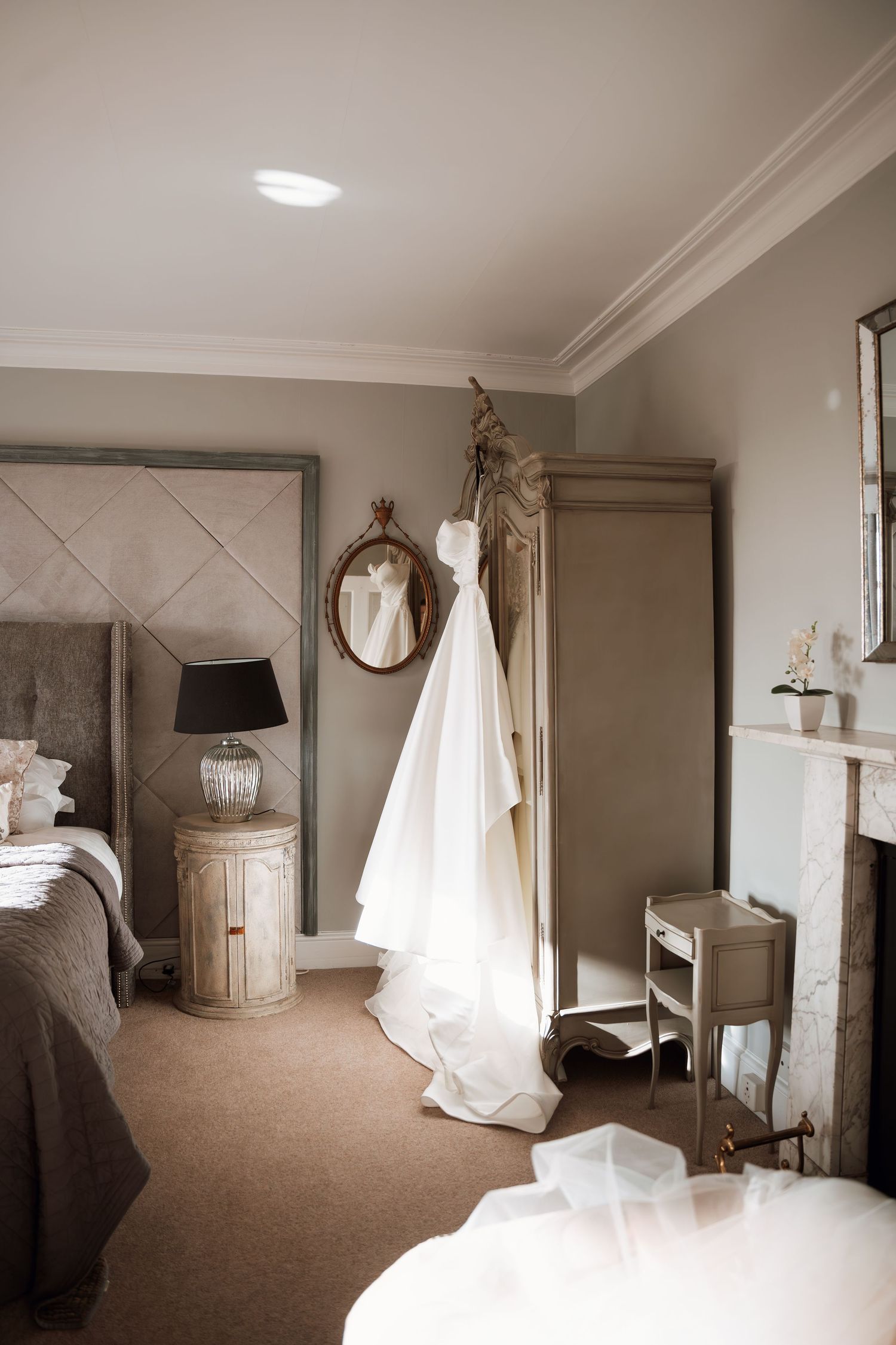 A serene bedroom with a white wedding dress hanging near an ornate mirror and vintage furniture.
