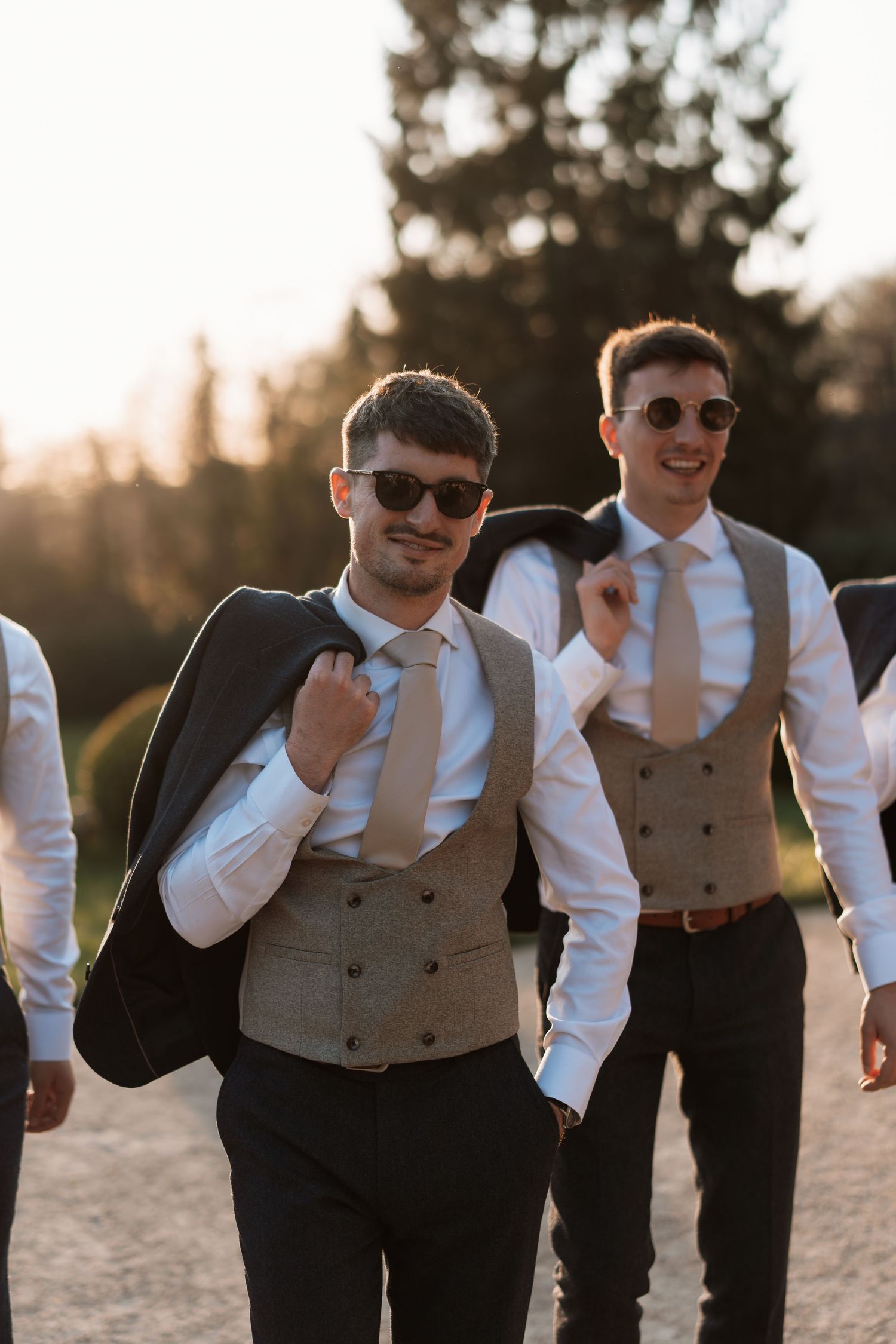 Groomsmen in matching attire and sunglasses smile during sunset at an outdoor wedding celebration.