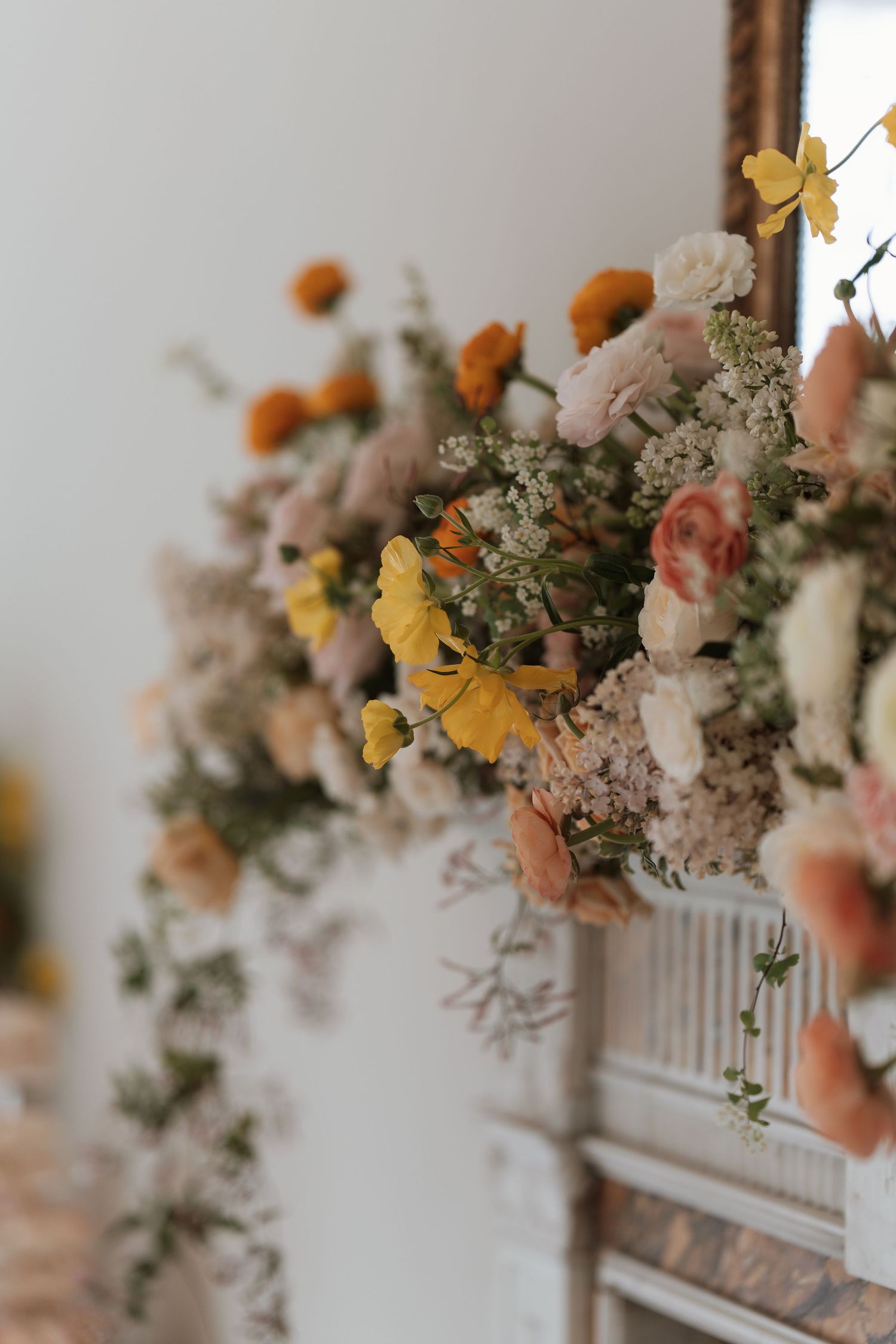 Romantic floral arrangement with peach, orange and yellow blooms on white mantle.
