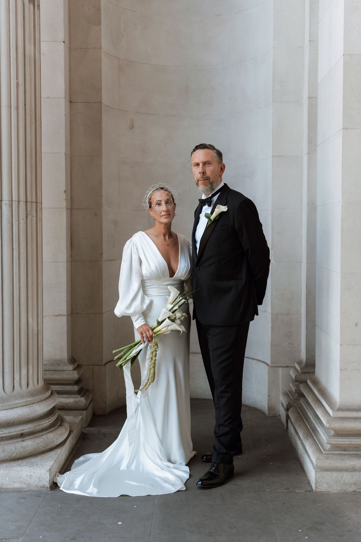 Wedding couple sharing intimate moment between grand white marble columns.