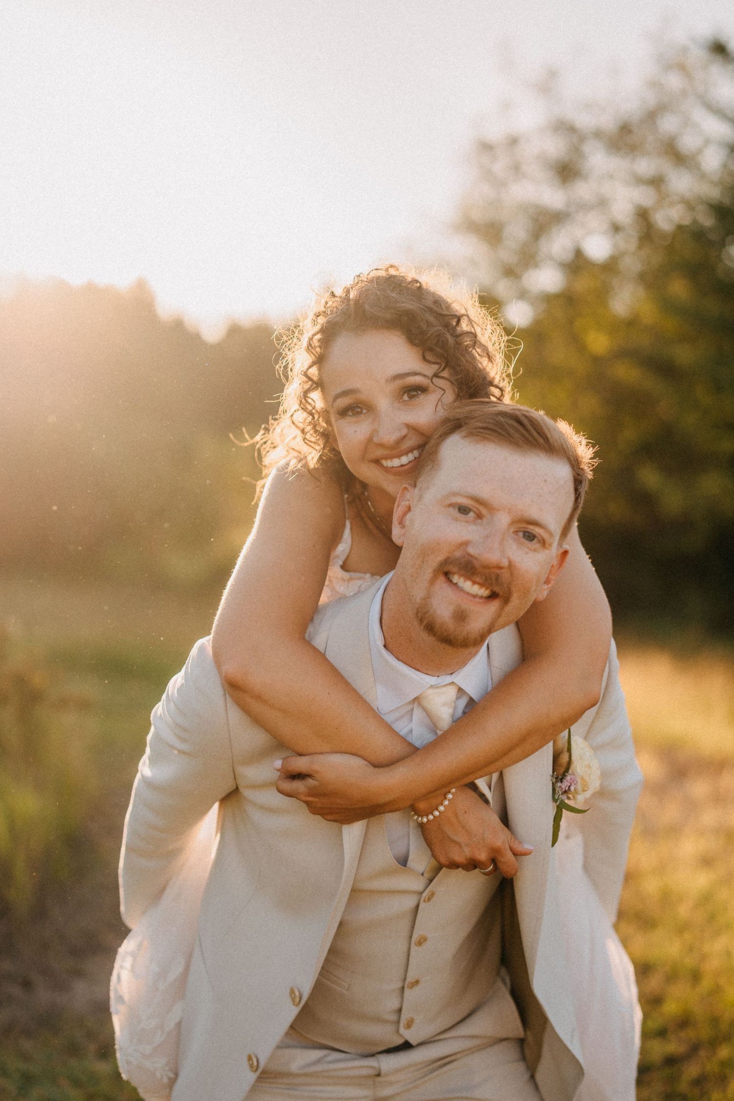 Joyful couple embraces in golden sunlit field during sunset wedding photoshoot.