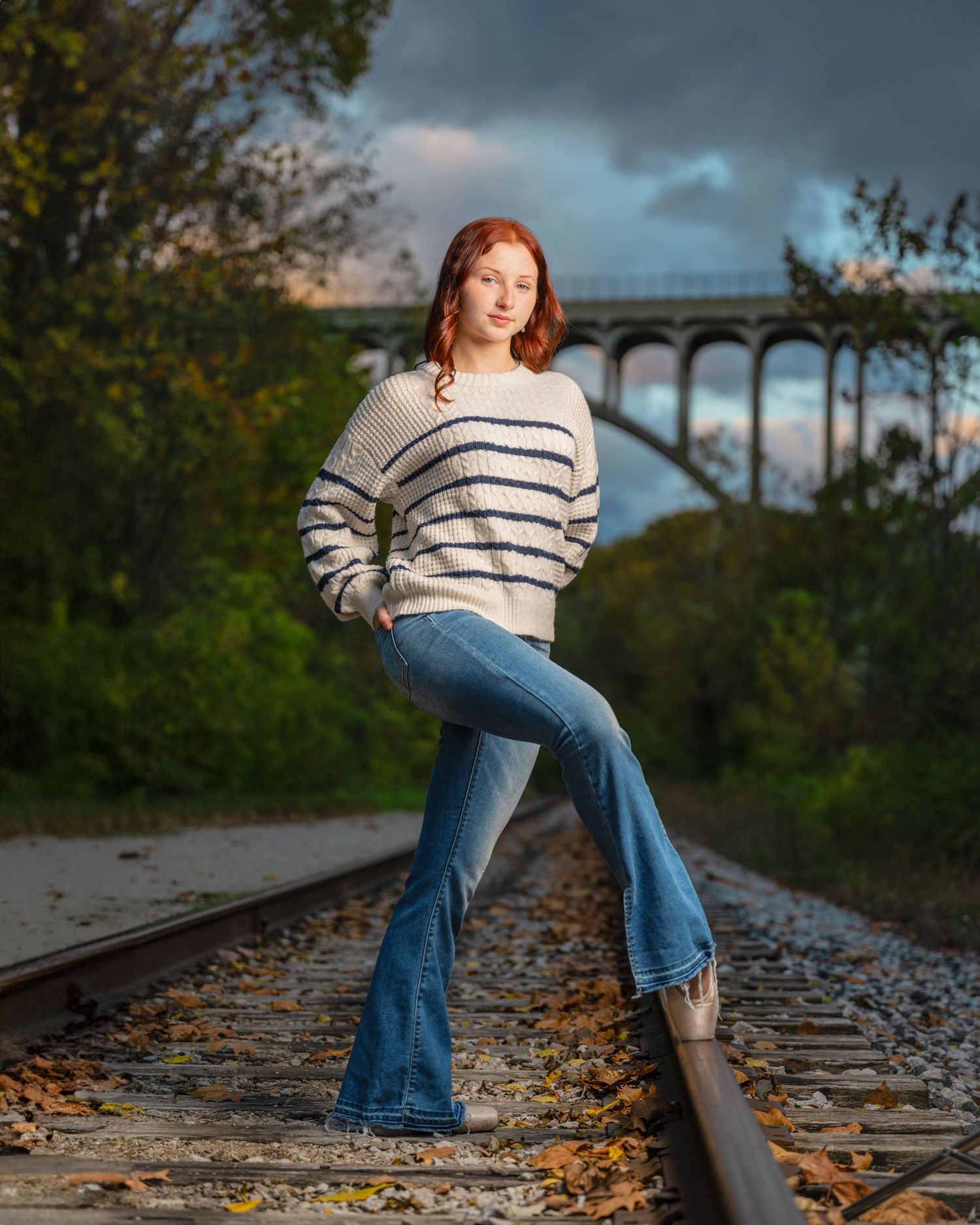 Casual autumn photoshoot on railroad tracks with fallen leaves.