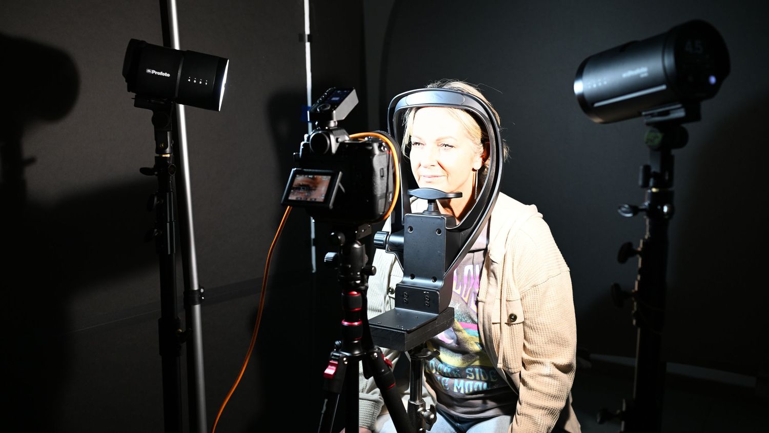Camera operator working with professional lighting equipment in dark studio setting.
