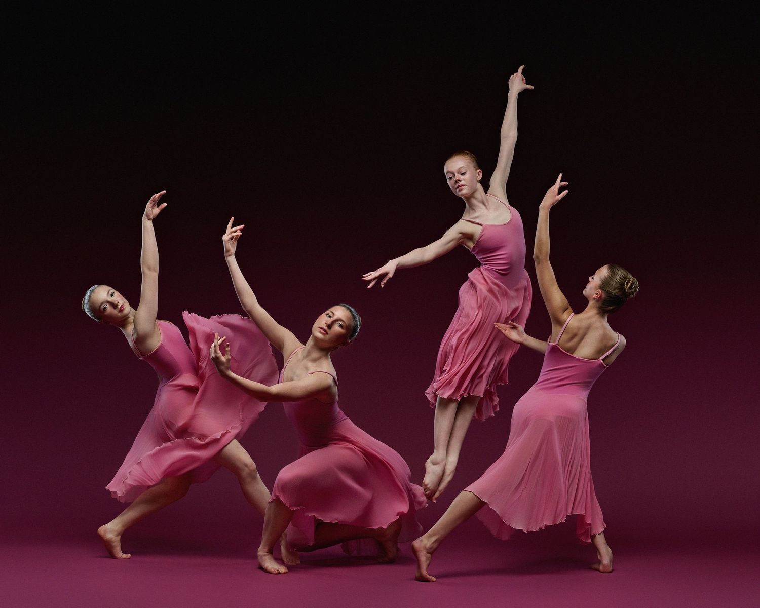 Modern dancers in flowing pink dresses performing expressive choreography.