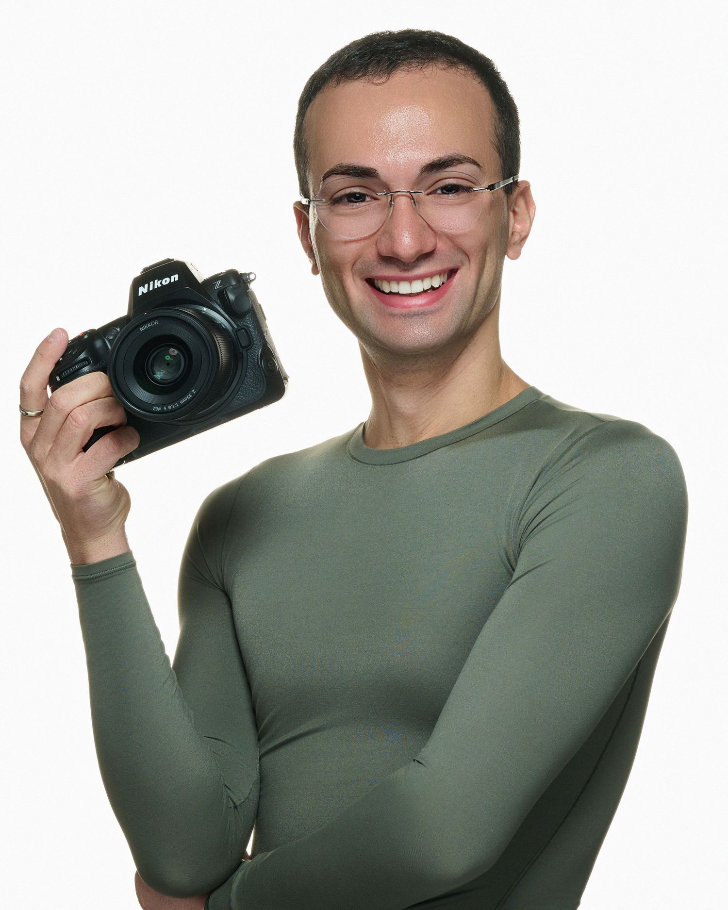 Portrait of a photographer wearing glasses and an olive green shirt holding a Nikon camera with a cheerful expression.
