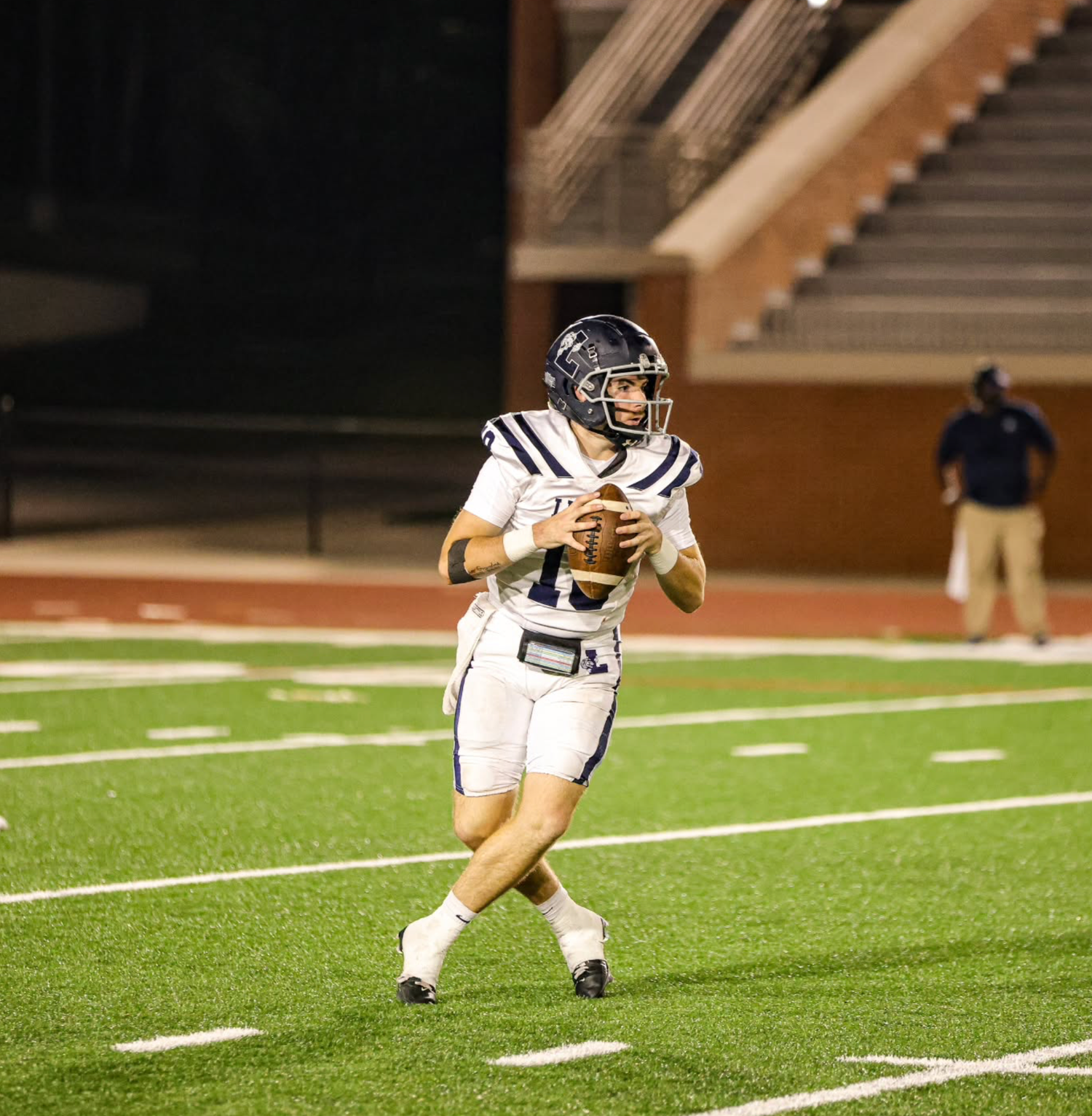 Football player in white uniform runs with ball on illuminated field at night.