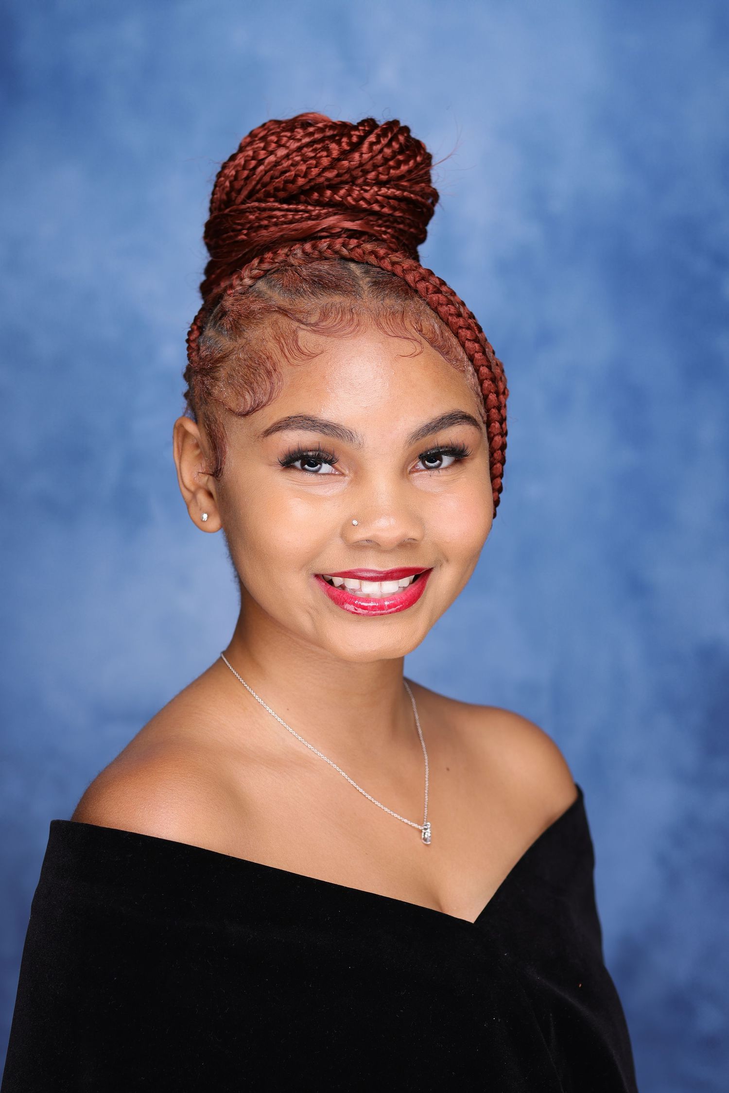 Portrait against blue background featuring braided updo hairstyle and off-shoulder top.
