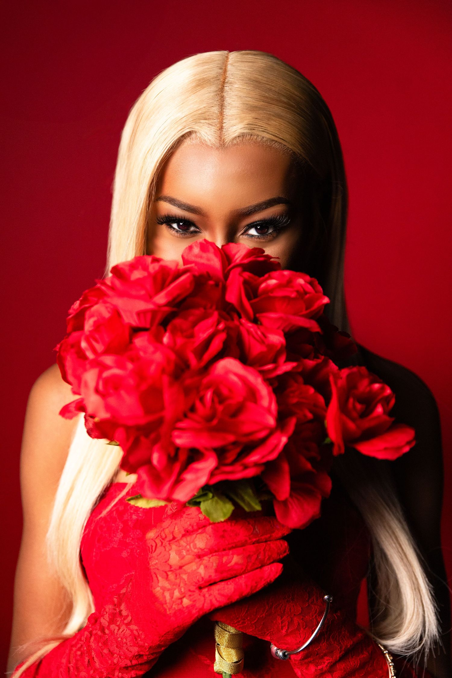 Portrait shot of someone holding vibrant red roses against a red background while wearing red gloves.