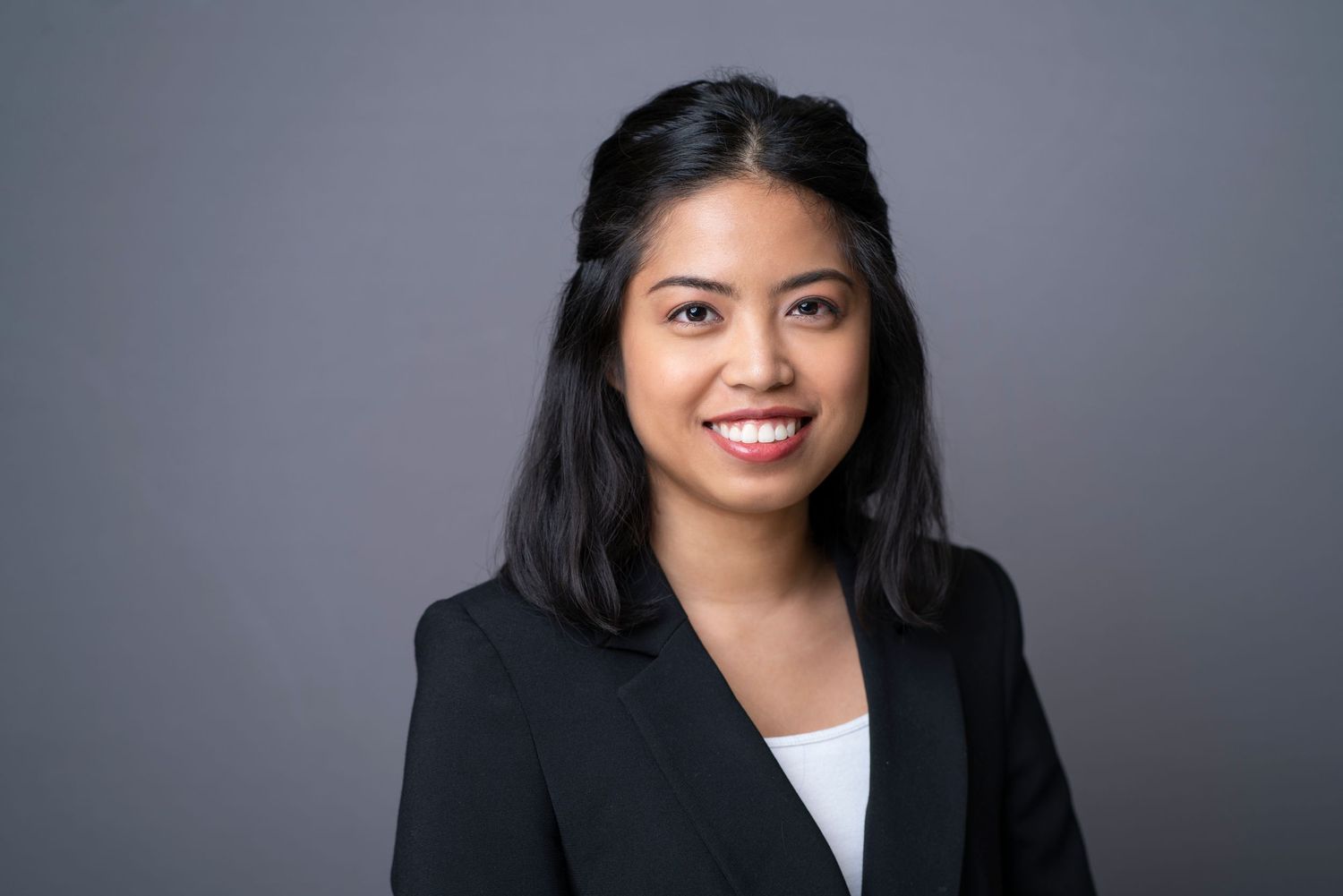 Professional headshot of businesswoman in black blazer against gray background.