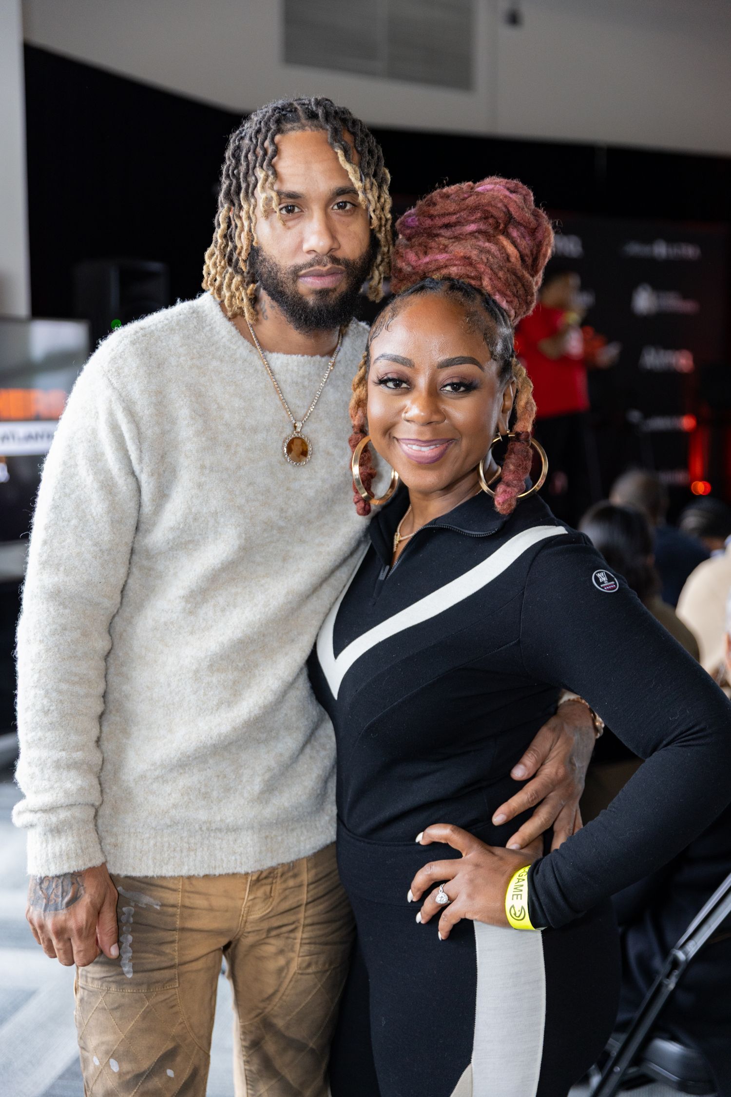 Two people in casual attire posing together at indoor event space.