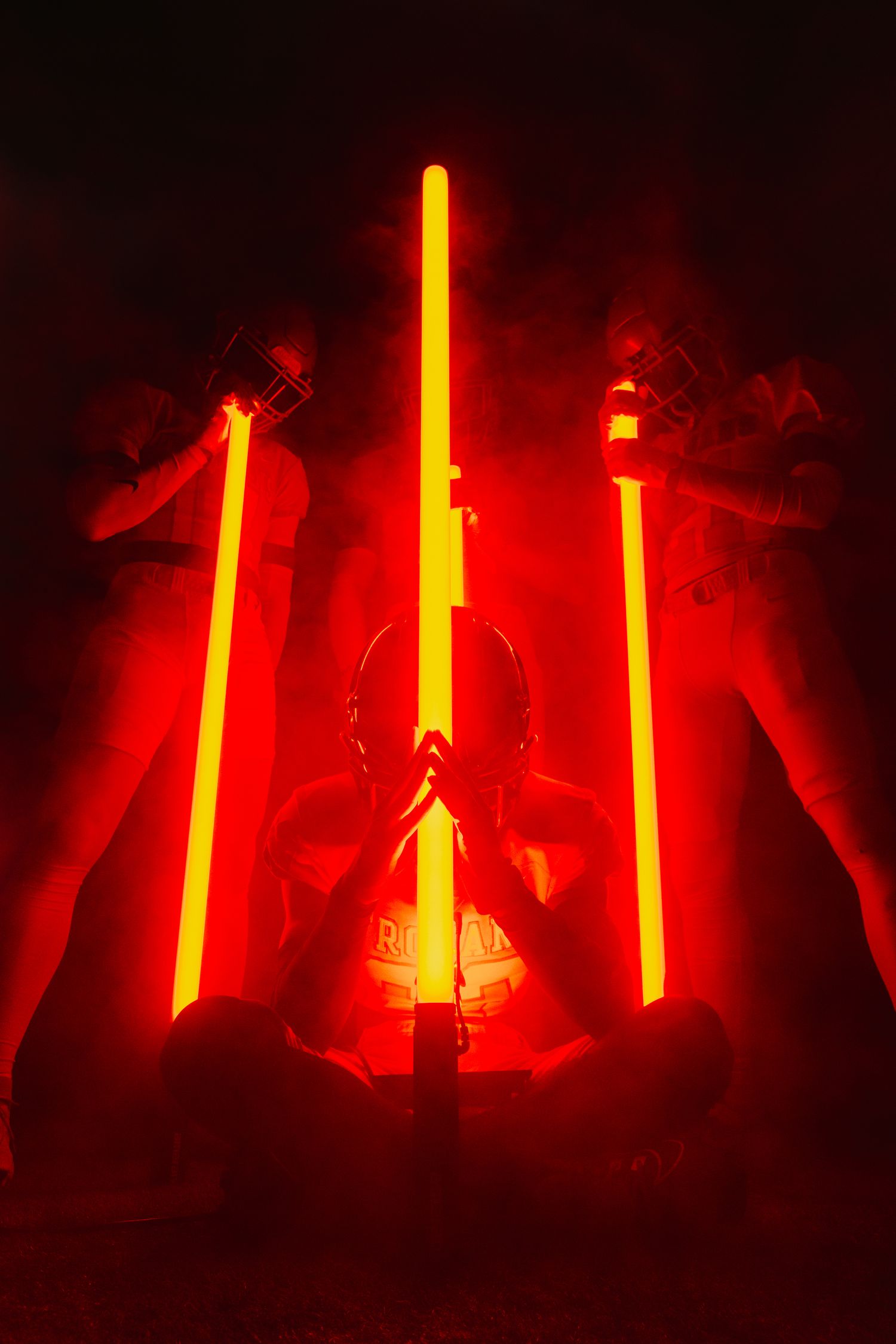 Football helmet silhouette surrounded by glowing red light bars in smoky atmosphere.