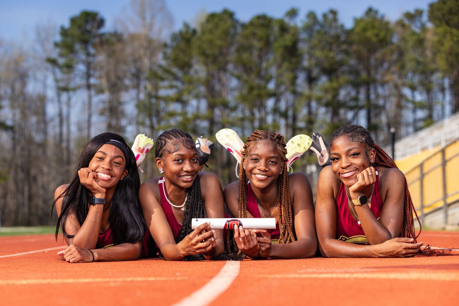 Four athletes in red uniforms lying on track surface smiling at camera.