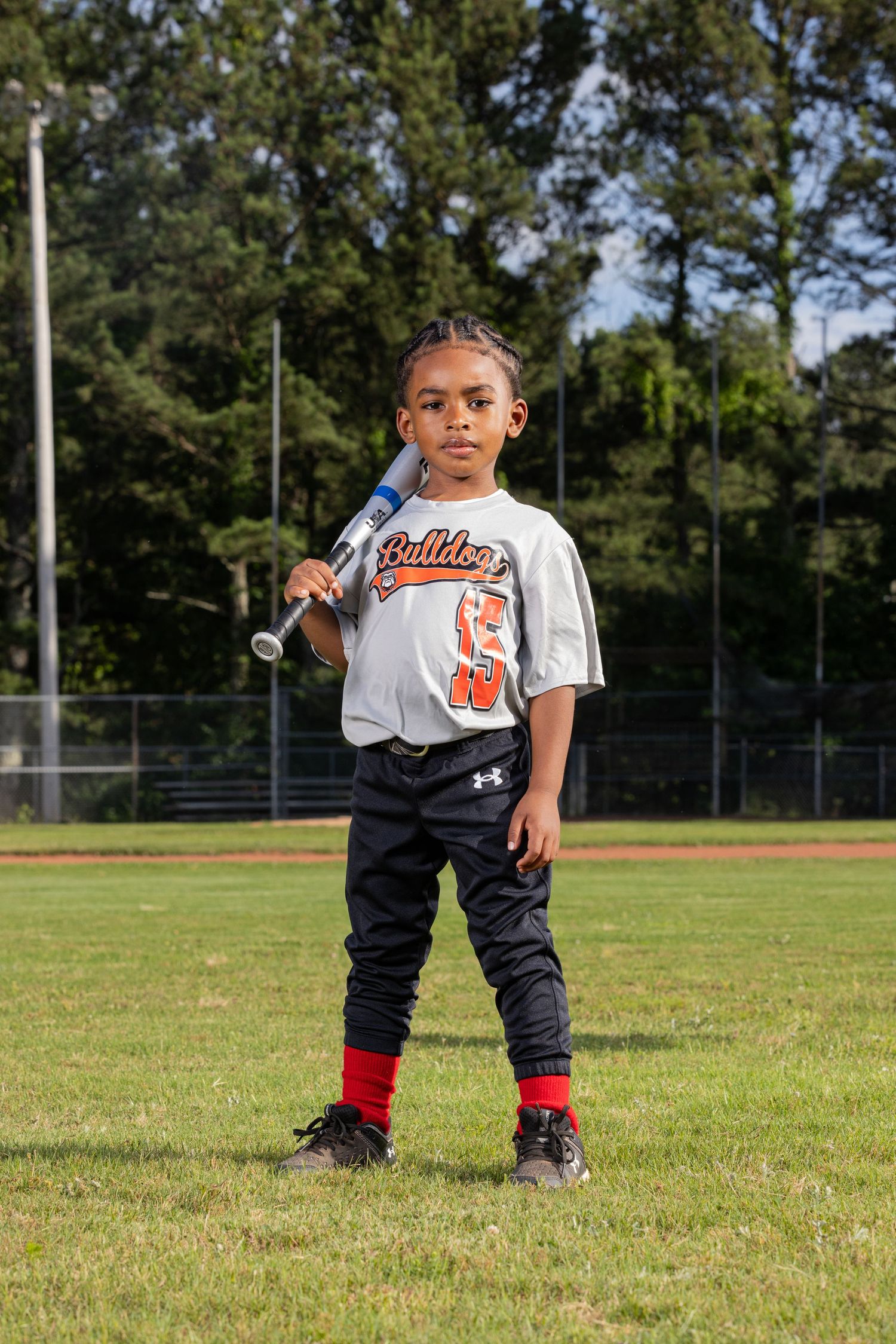 Youth baseball player poses on field in white jersey and black pants with bat over shoulder.