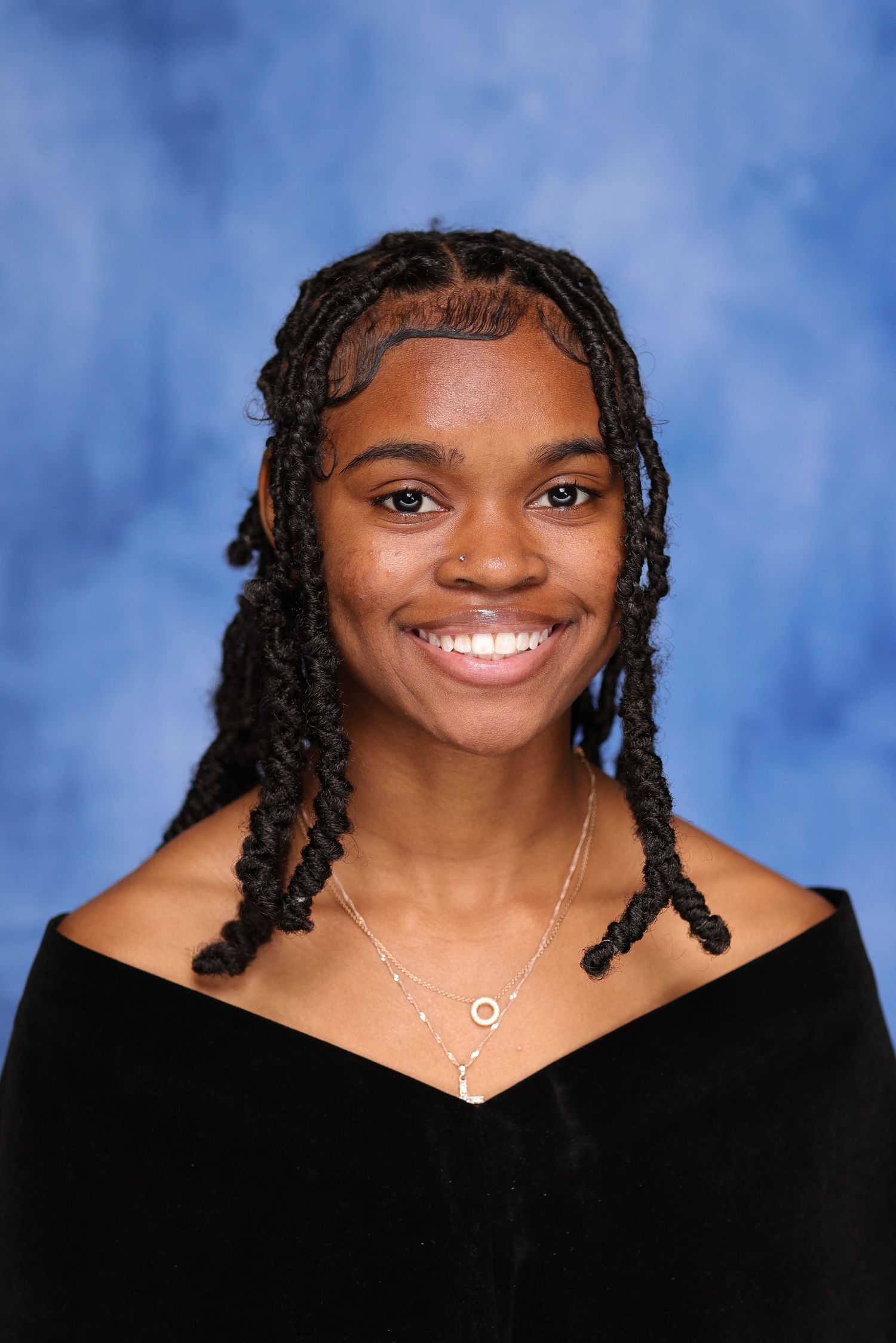 Studio portrait with braided hairstyle and off-shoulder black top against blue background.