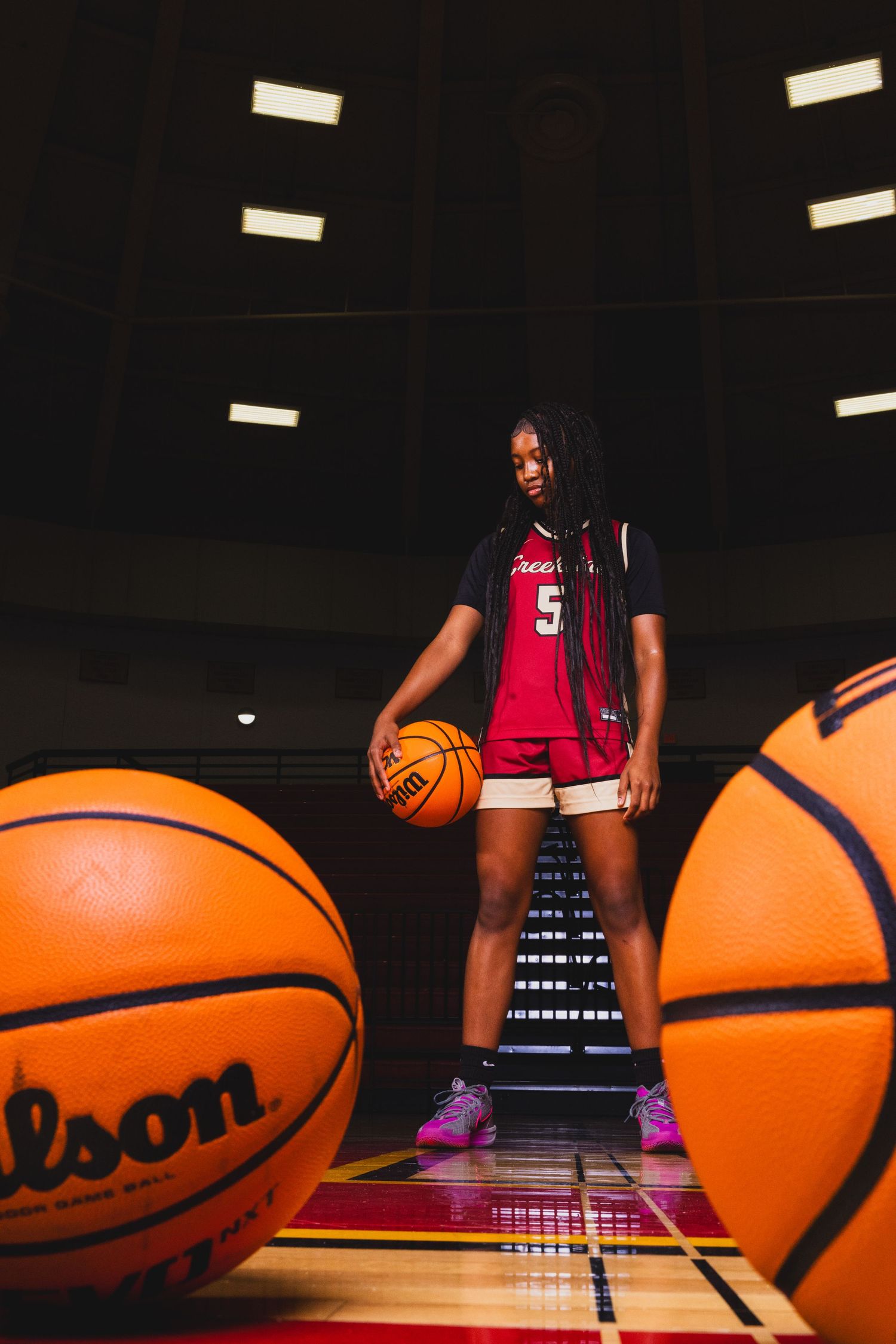 Basketball player in red jersey poses with Wilson basketball on court with dramatic lighting.