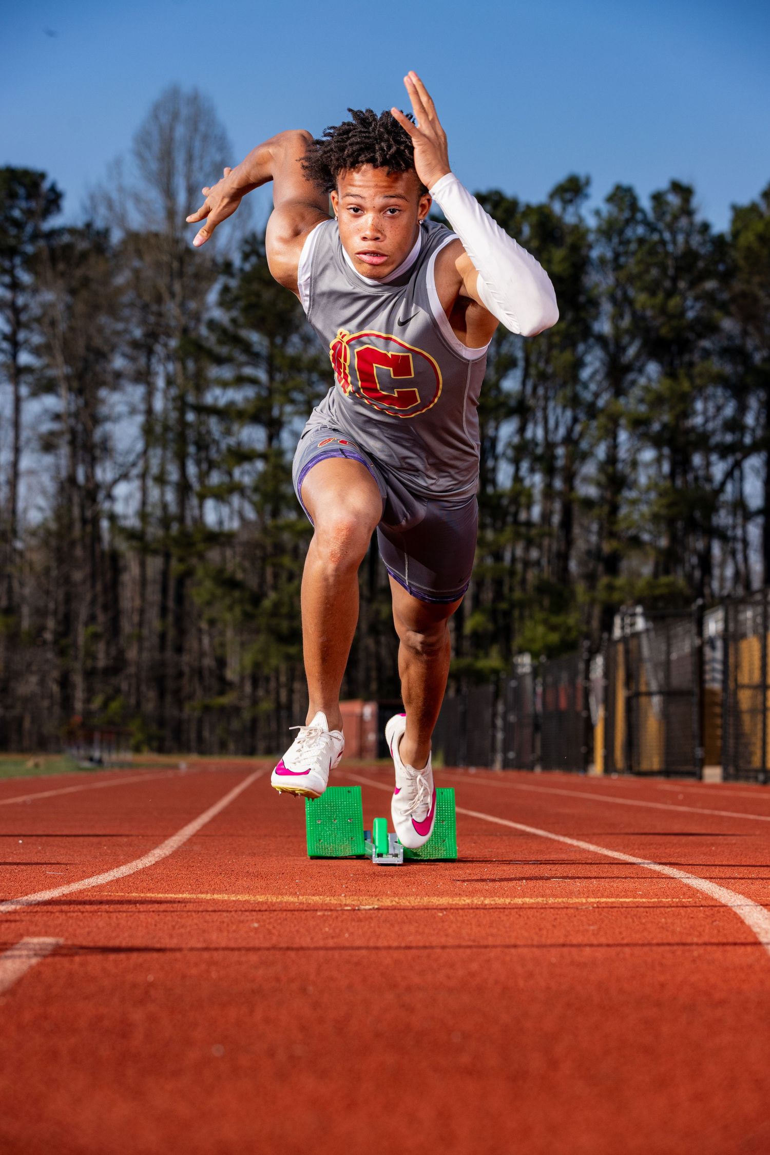 Athlete in grey uniform launching from starting block on running track.