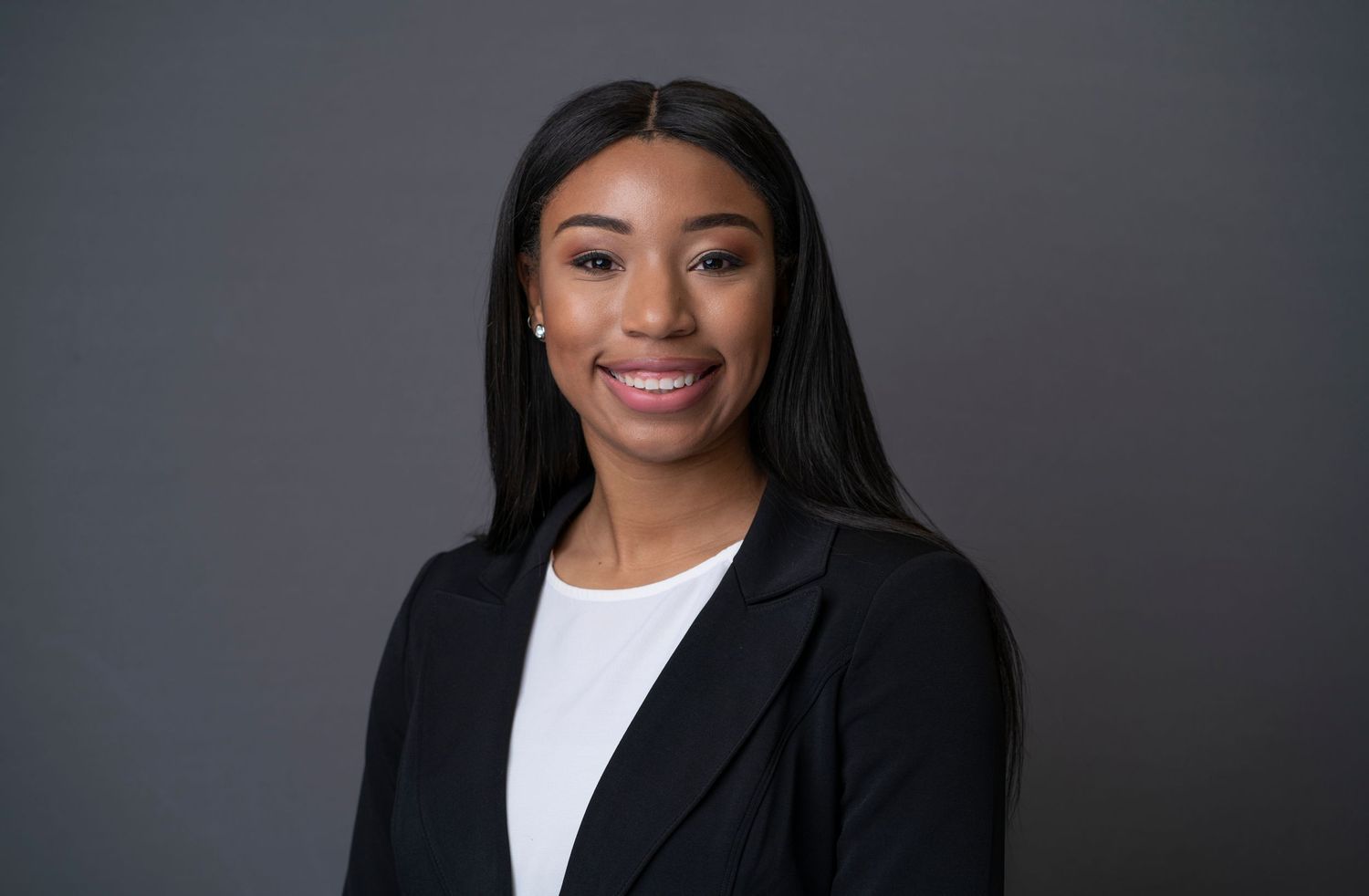 Corporate headshot of businesswoman in black suit against neutral background.