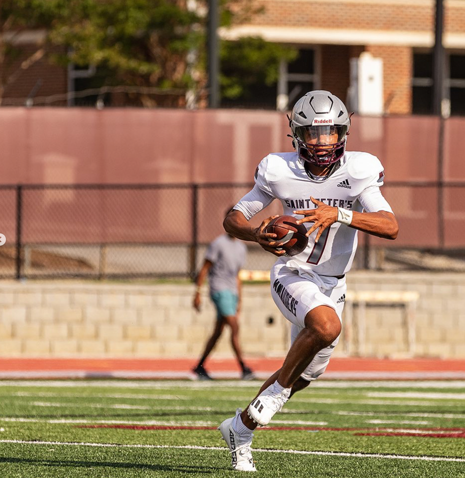 Football player in white uniform runs with ball during game on turf field.