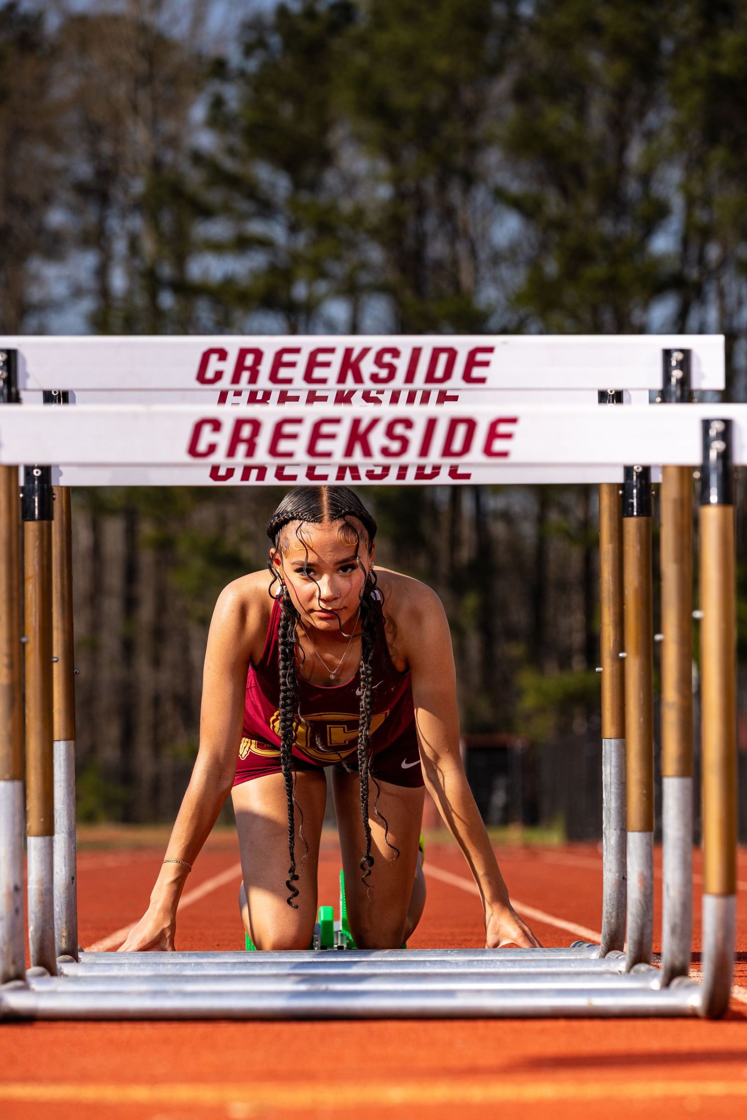 Track athlete in starting position under Creekside hurdles on running track.