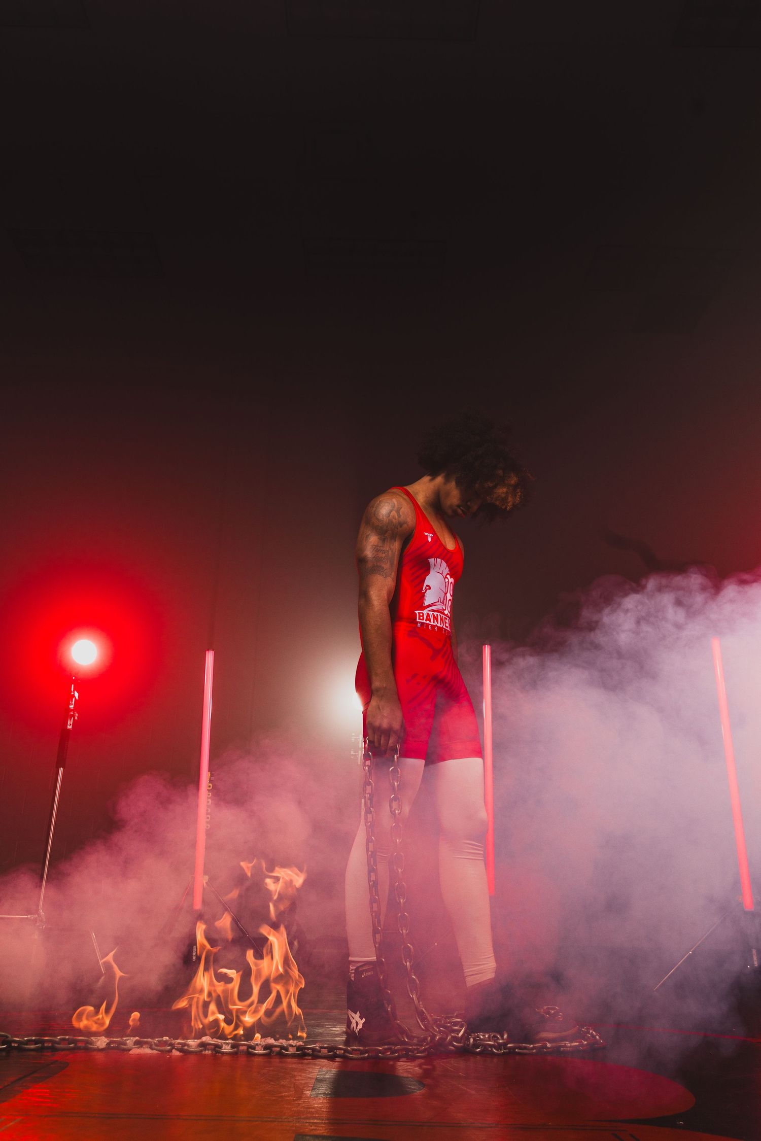 Silhouetted performer in red jersey stands amid smoke and fire effects on stage.