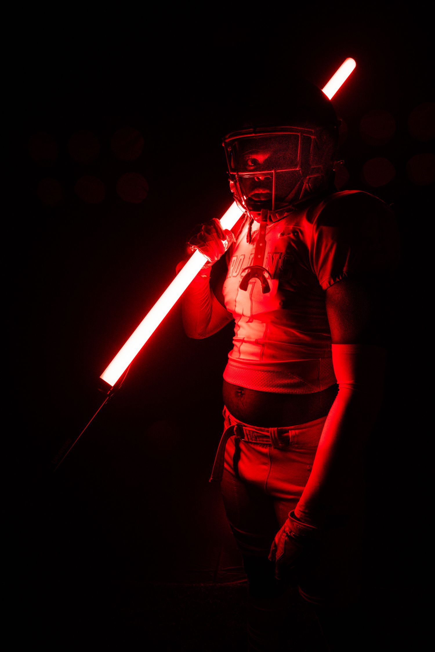 Figure in football gear poses with glowing red light bar against dark background.