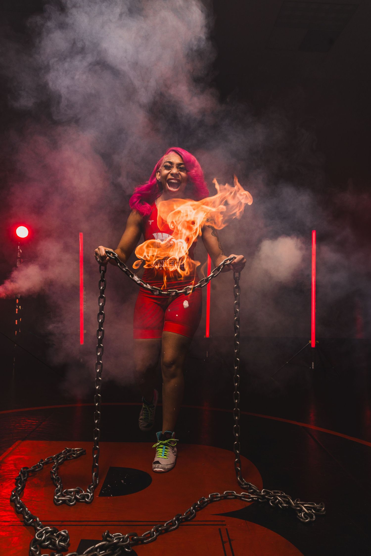 Performer in red outfit stands with chains in dramatic smoke and lighting.