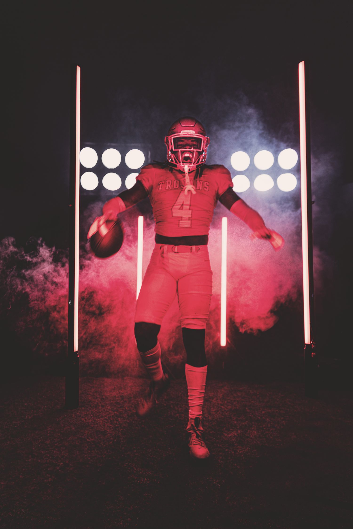 Football player in red uniform stands dramatically in front of bright stadium lights with smoke effects.