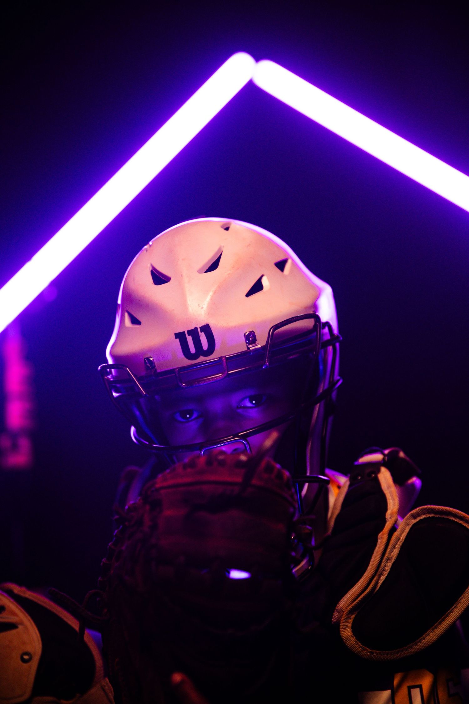 Baseball helmet illuminated by neon purple lighting creates dramatic sports portrait.