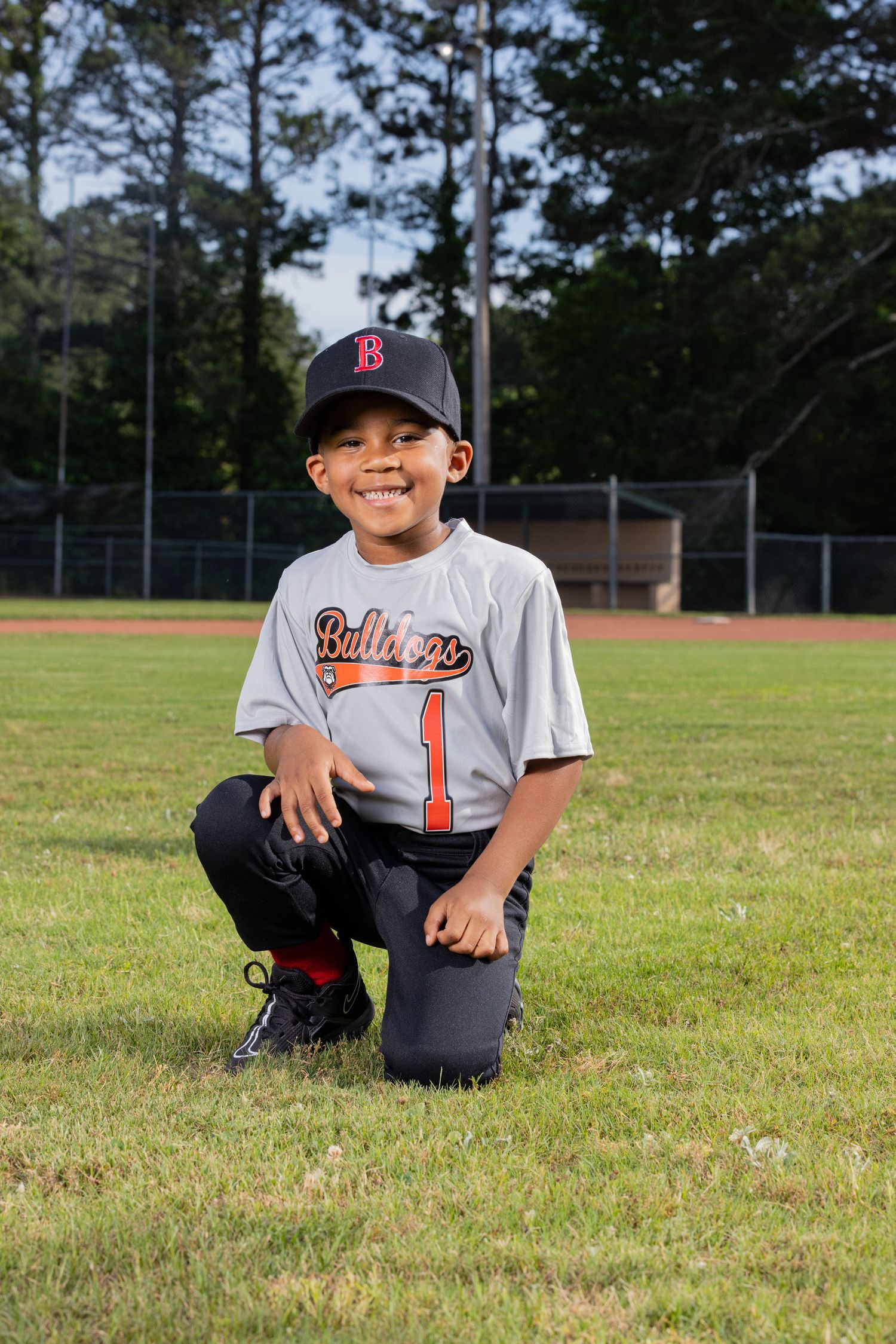 Youth baseball player in Red Sox uniform kneels on baseball field.