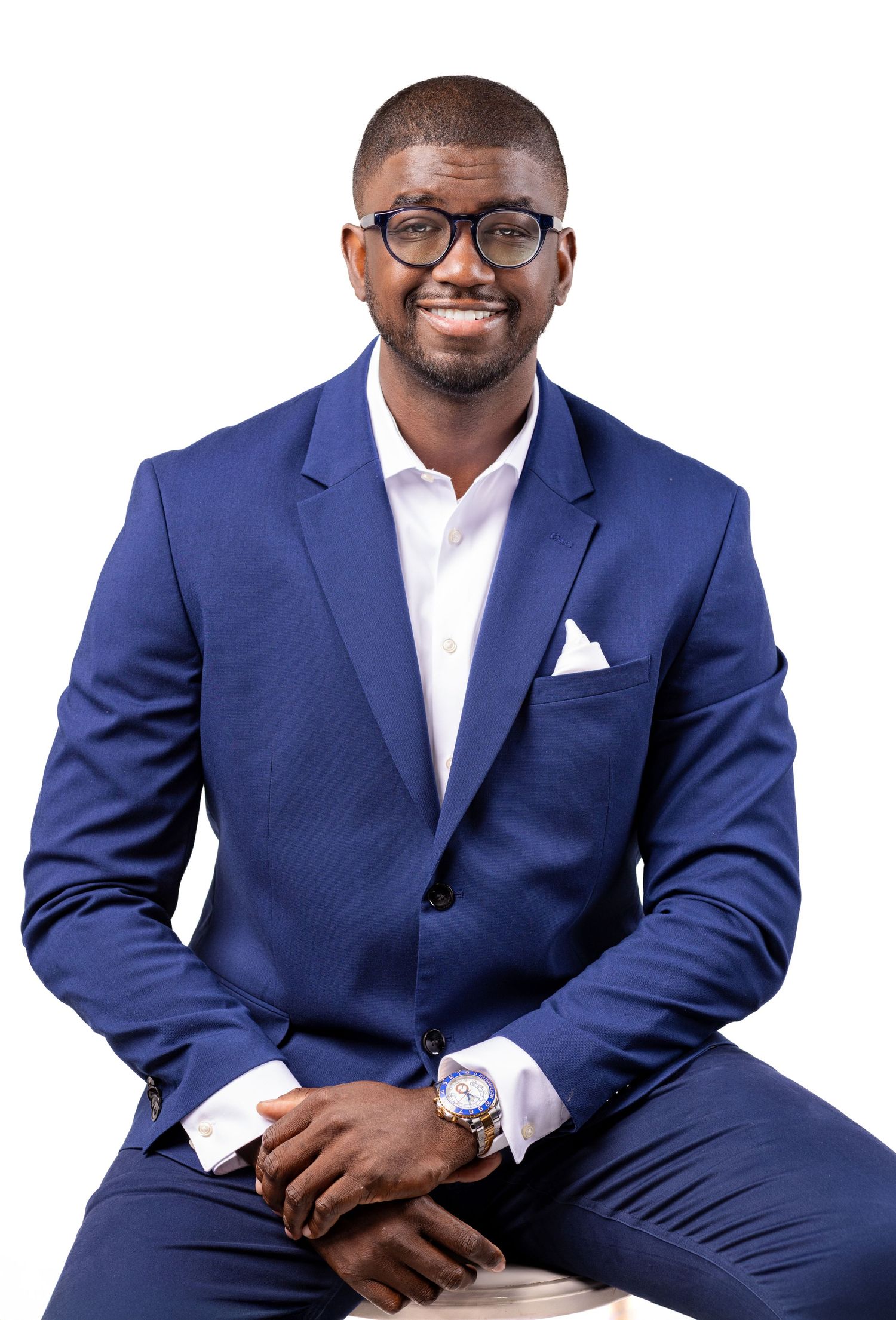 Professional headshot of man in navy blue suit and glasses against light background.