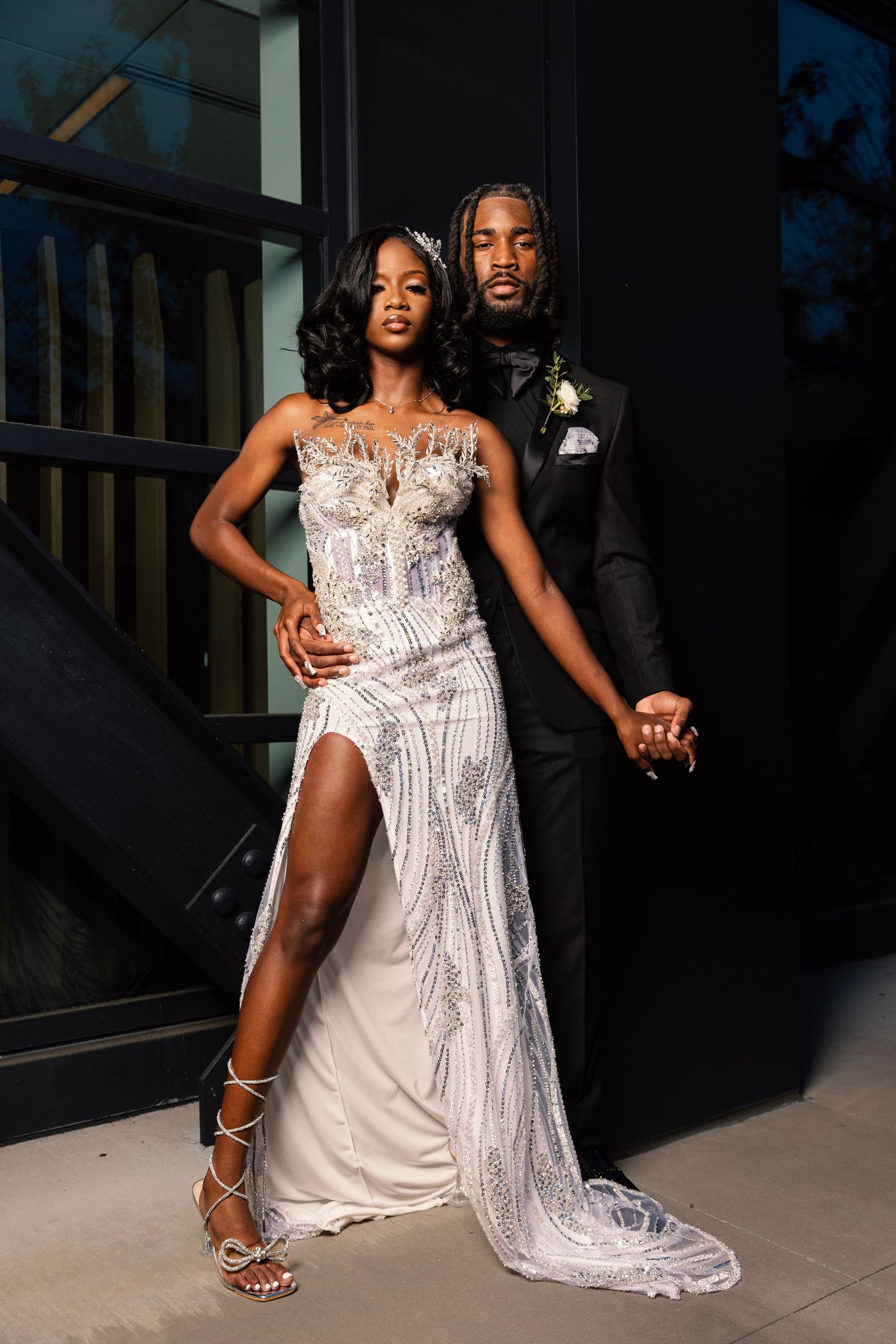 Couple in formal attire posing for elegant photo, woman wearing white beaded gown.