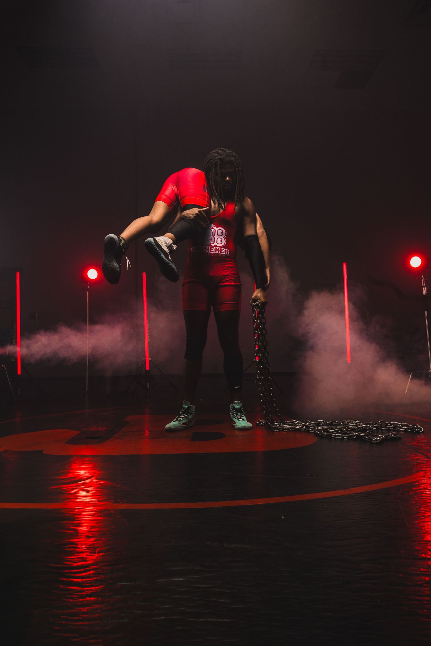 Athletic figure in red shirt poses with chains in dramatic lighting with red smoke effects and spotlights.