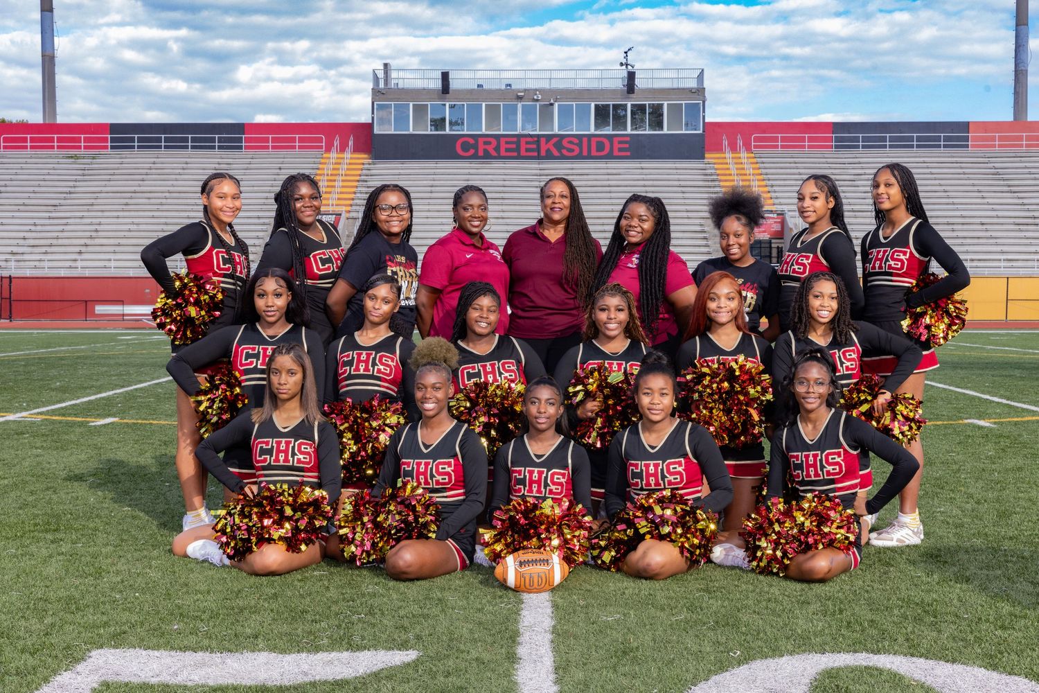 Cheerleading squad in black uniforms poses for team photo on football field.