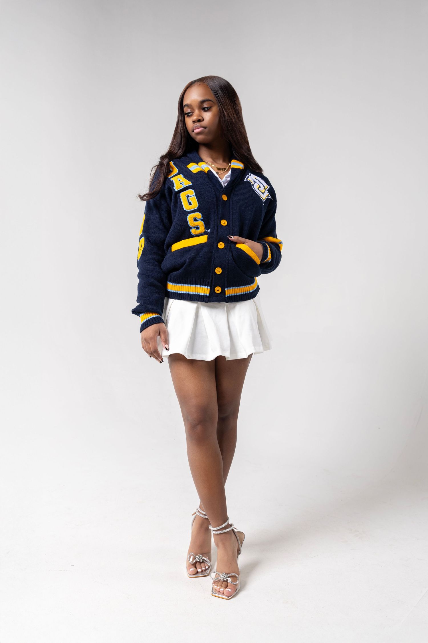 A varsity letterman jacket styled with a white skirt and high heels in a studio setting.