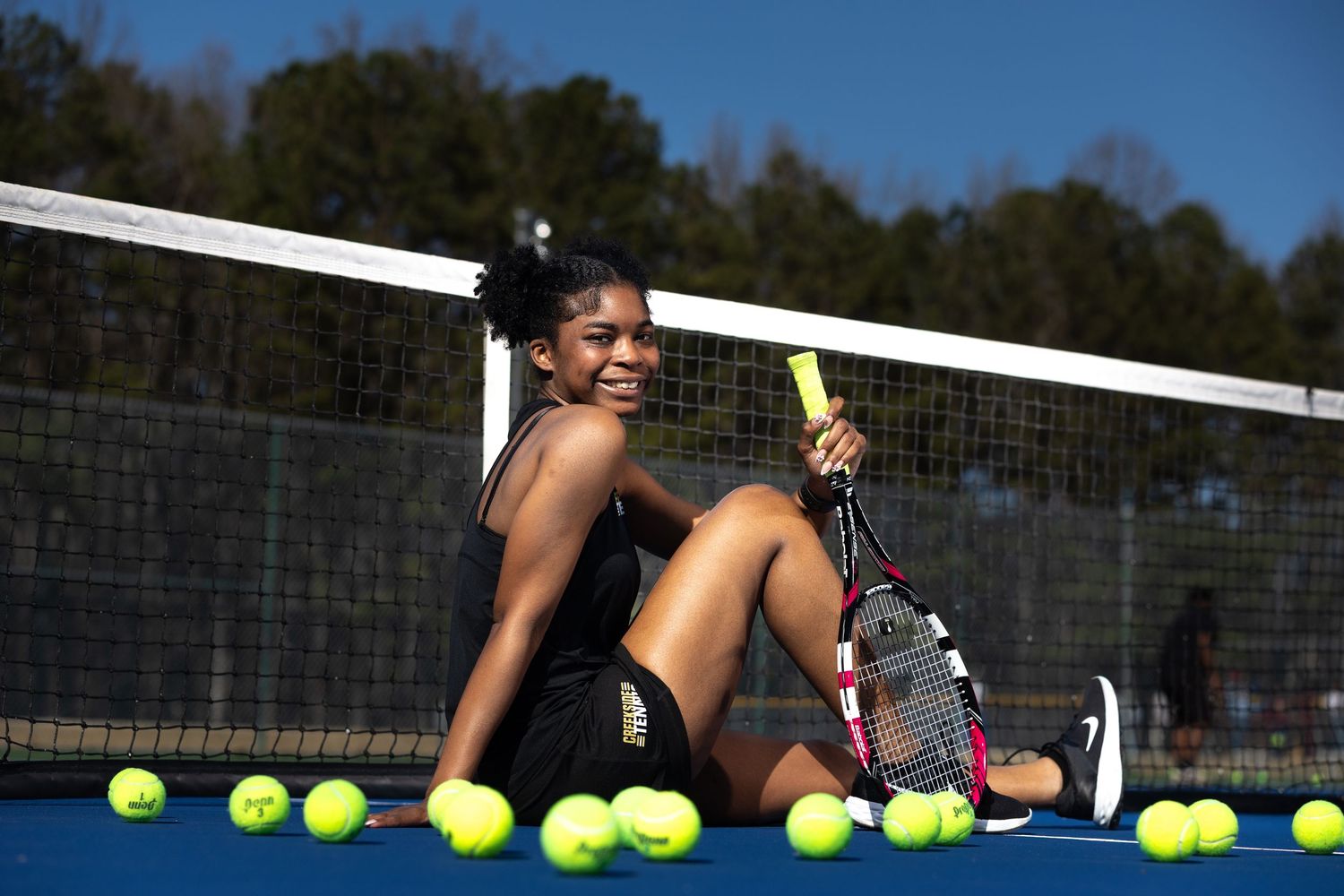 Tennis player sits surrounded by yellow tennis balls on a blue court.