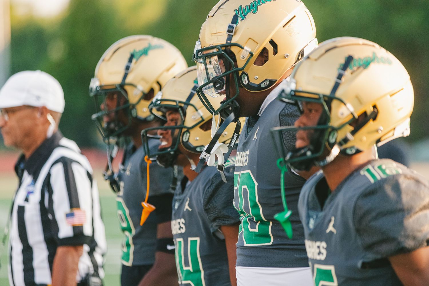 College football players in green and gold uniforms line up during a game with a referee in the background.