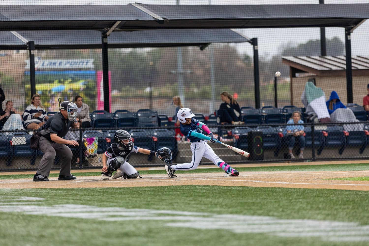 Baseball player in mid-swing at bat during a game with umpire and catcher visible.