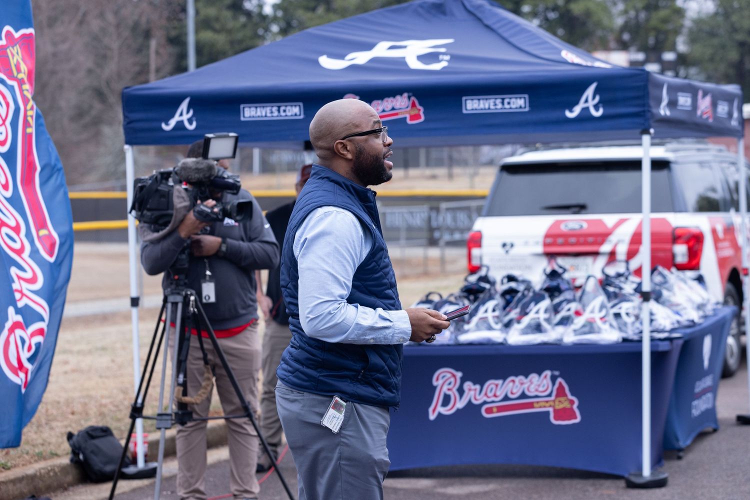 Camera crew and merchandise tent at Atlanta Braves promotional event with blue canopy tent and display table.
