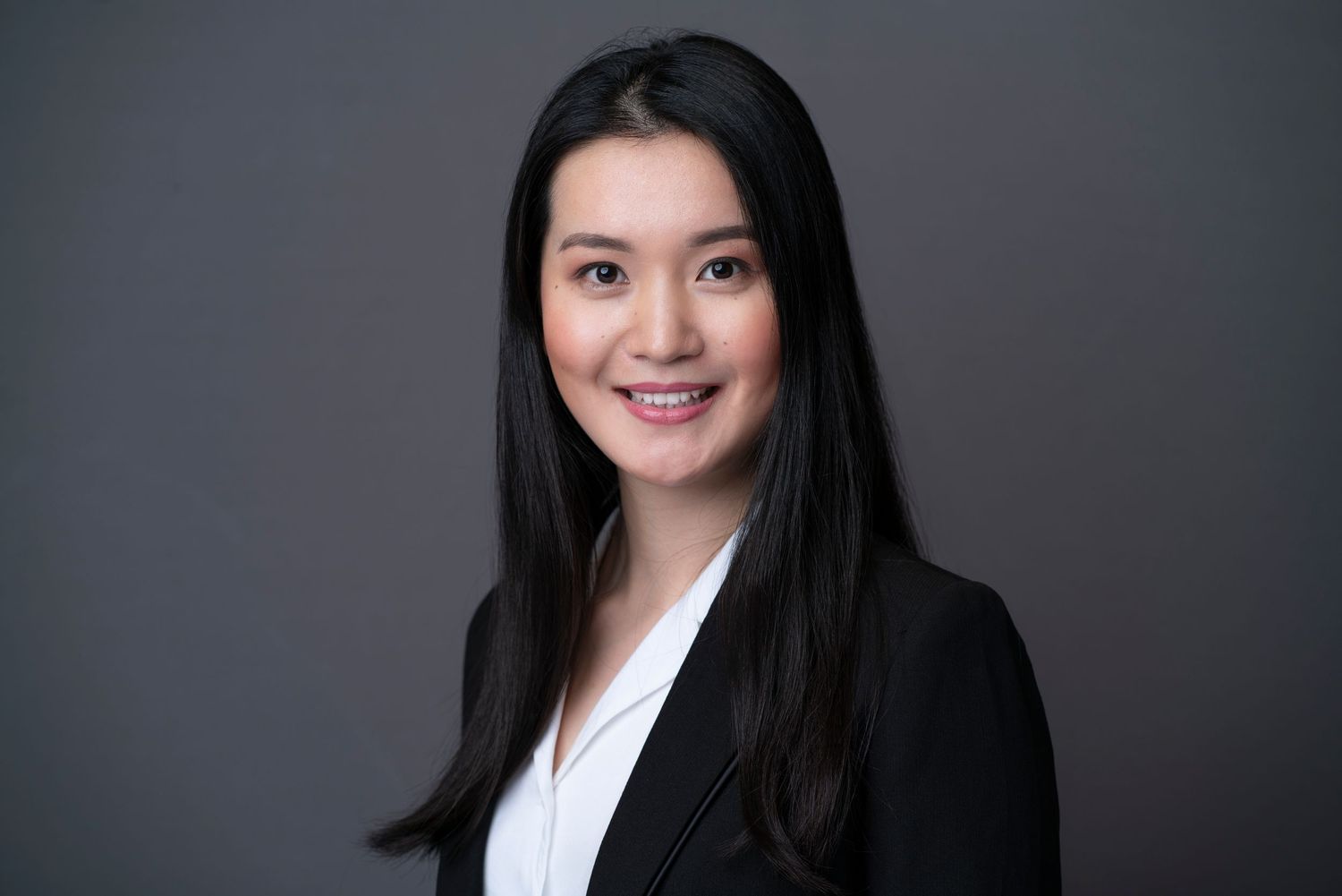 Corporate headshot of businesswoman in black blazer against gray background.