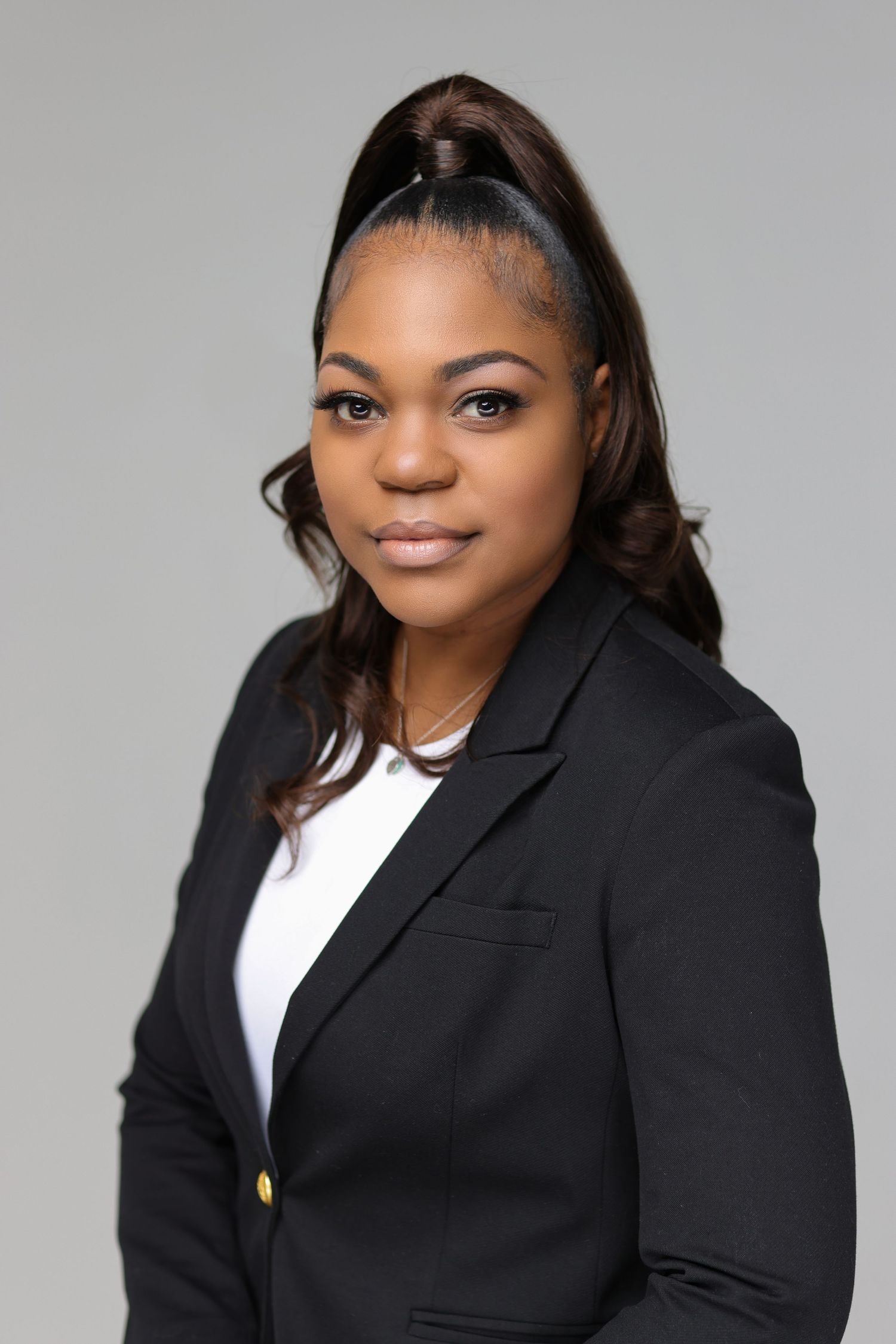 Professional headshot in black blazer and white blouse against grey background.