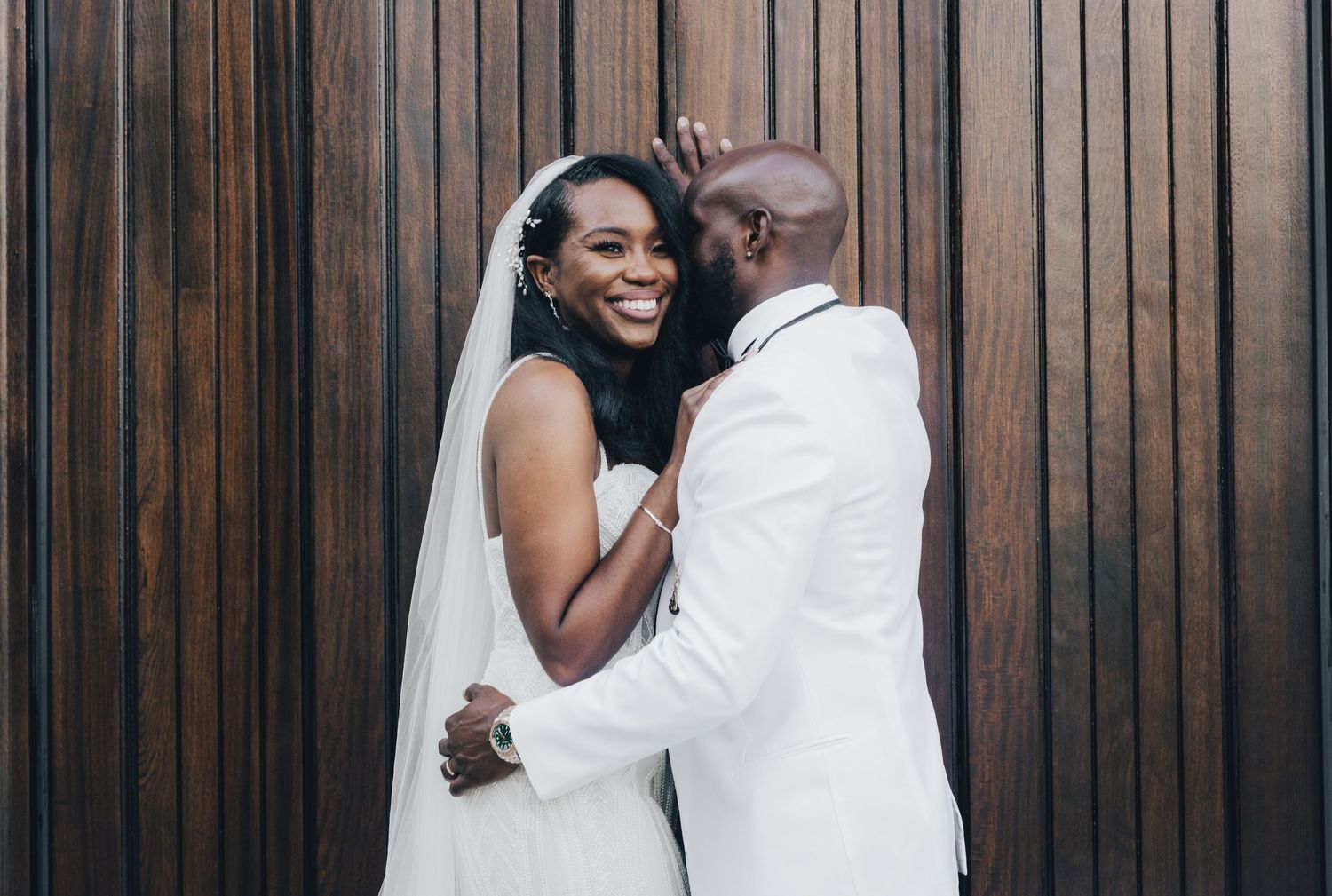 Wedding couple sharing intimate moment against wooden panel wall.