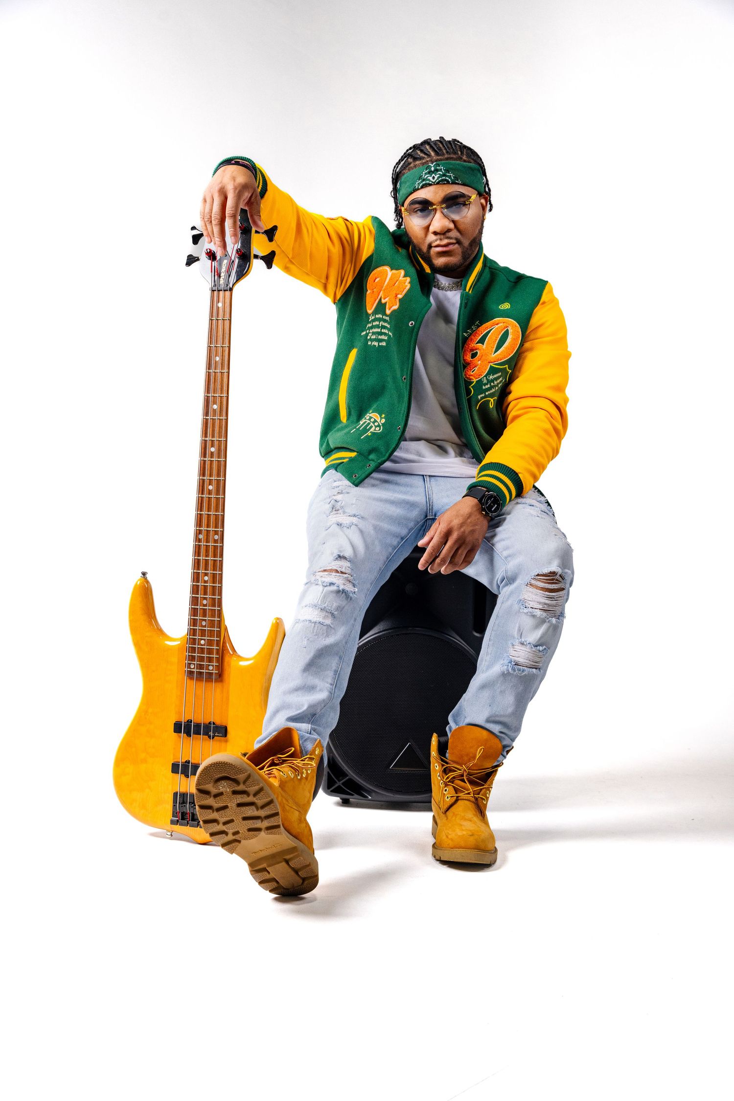 Musician poses with yellow bass guitar wearing green and yellow varsity jacket and ripped jeans.