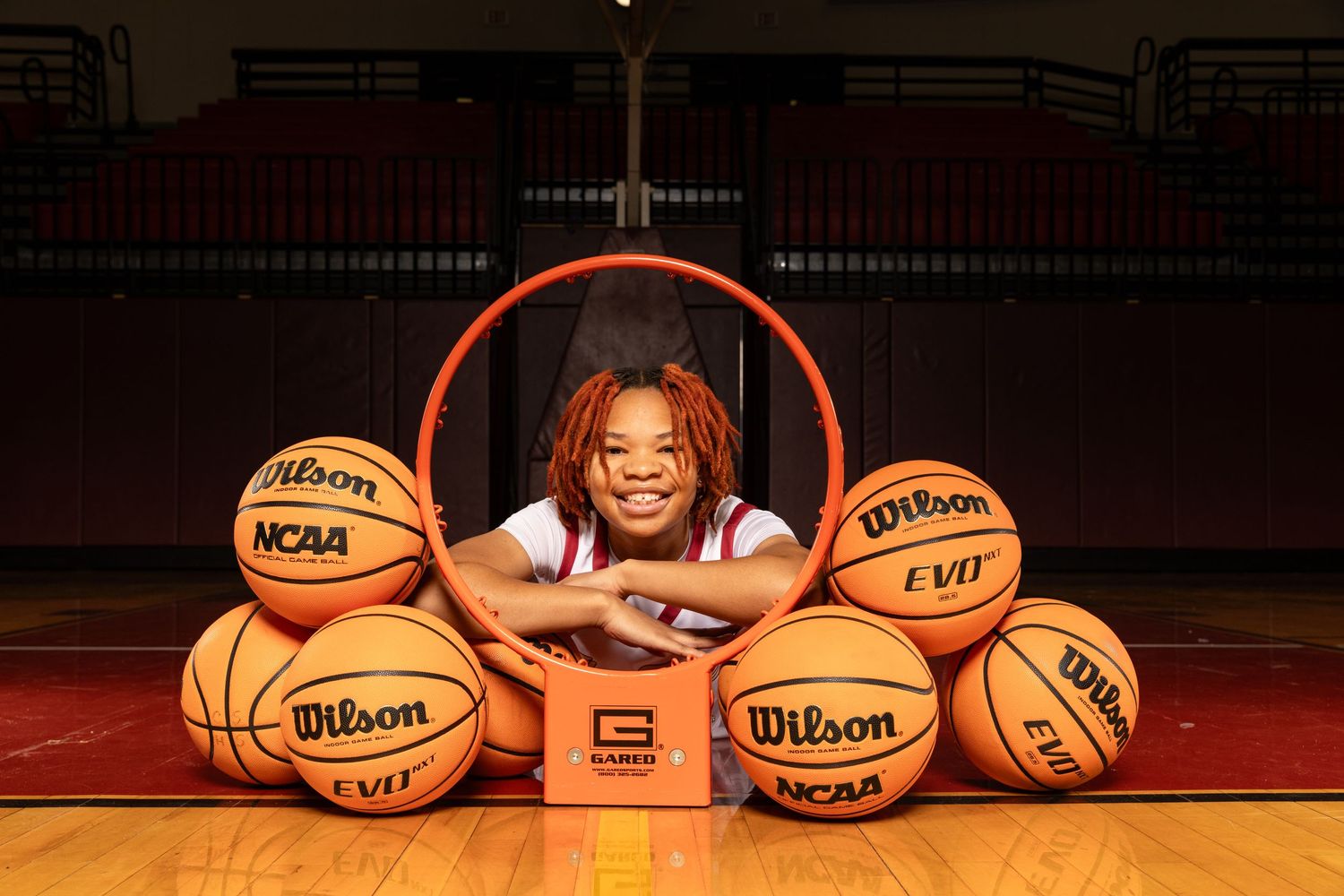 Basketball player posing with multiple Wilson NCAA basketballs on a gym court.