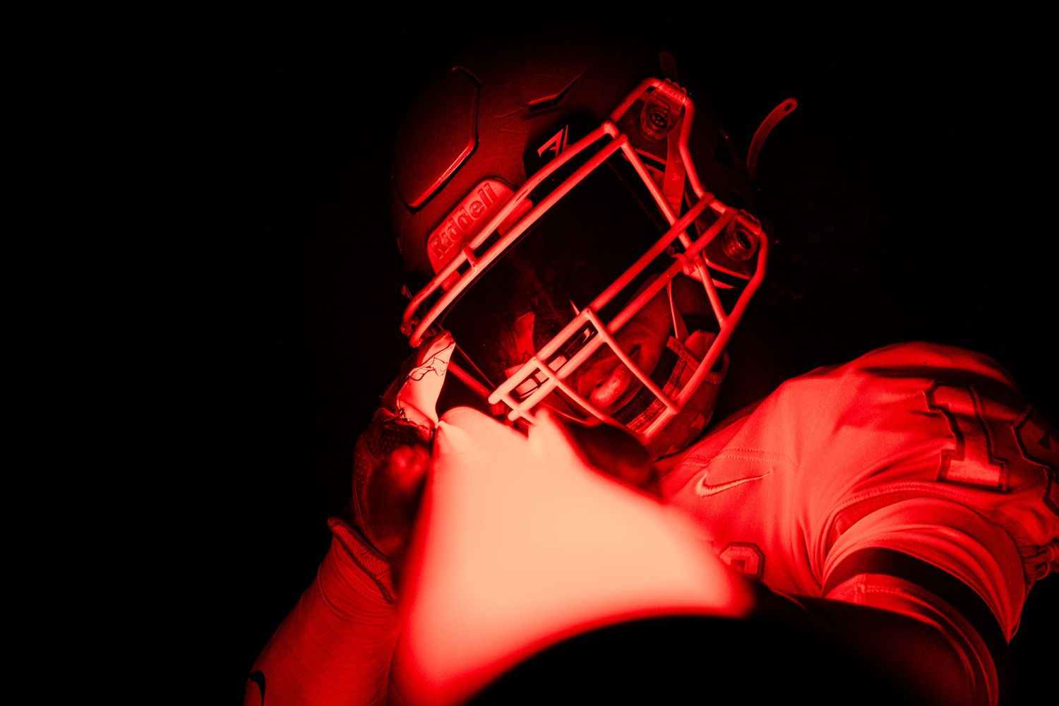Close-up shot of football helmet illuminated in dramatic red lighting.