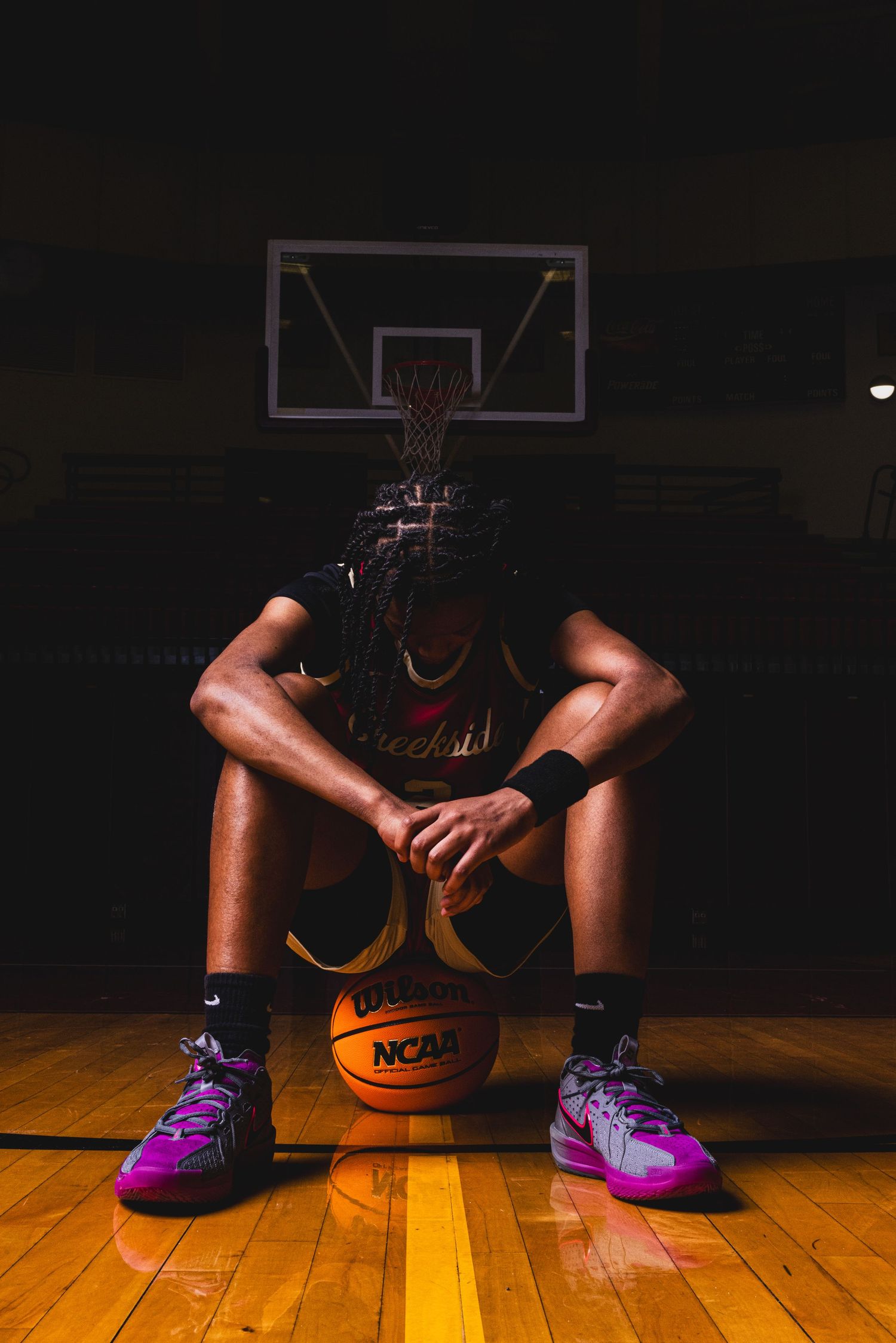 Player sits on basketball court with NCAA ball in foreground and hoop visible in background.