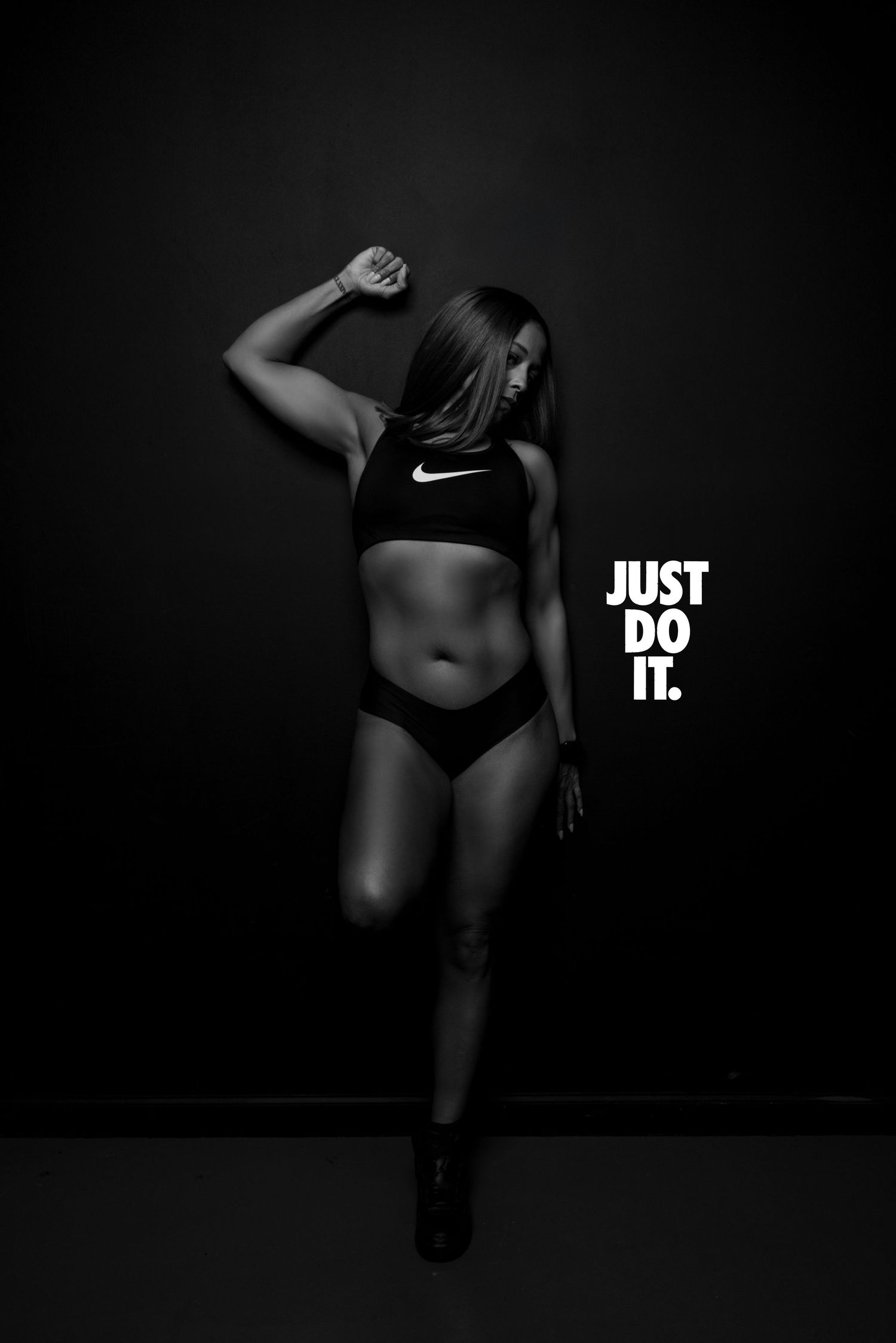 Dramatic black and white fitness portrait with Nike slogan against dark background.