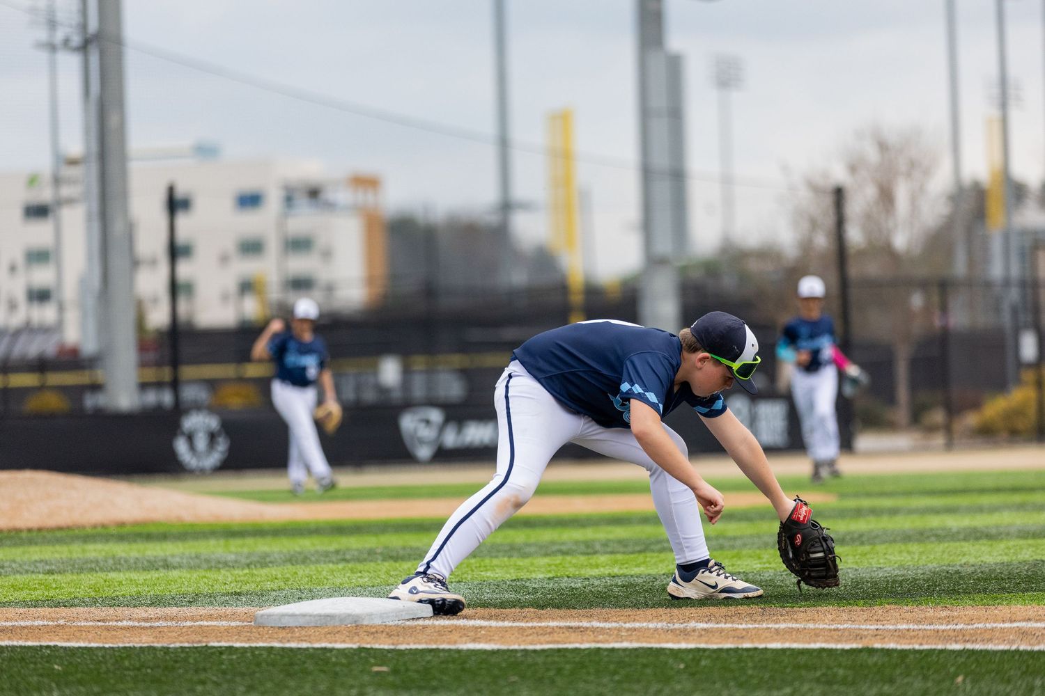 Baseball infielder in navy uniform crouches in ready position on the field.