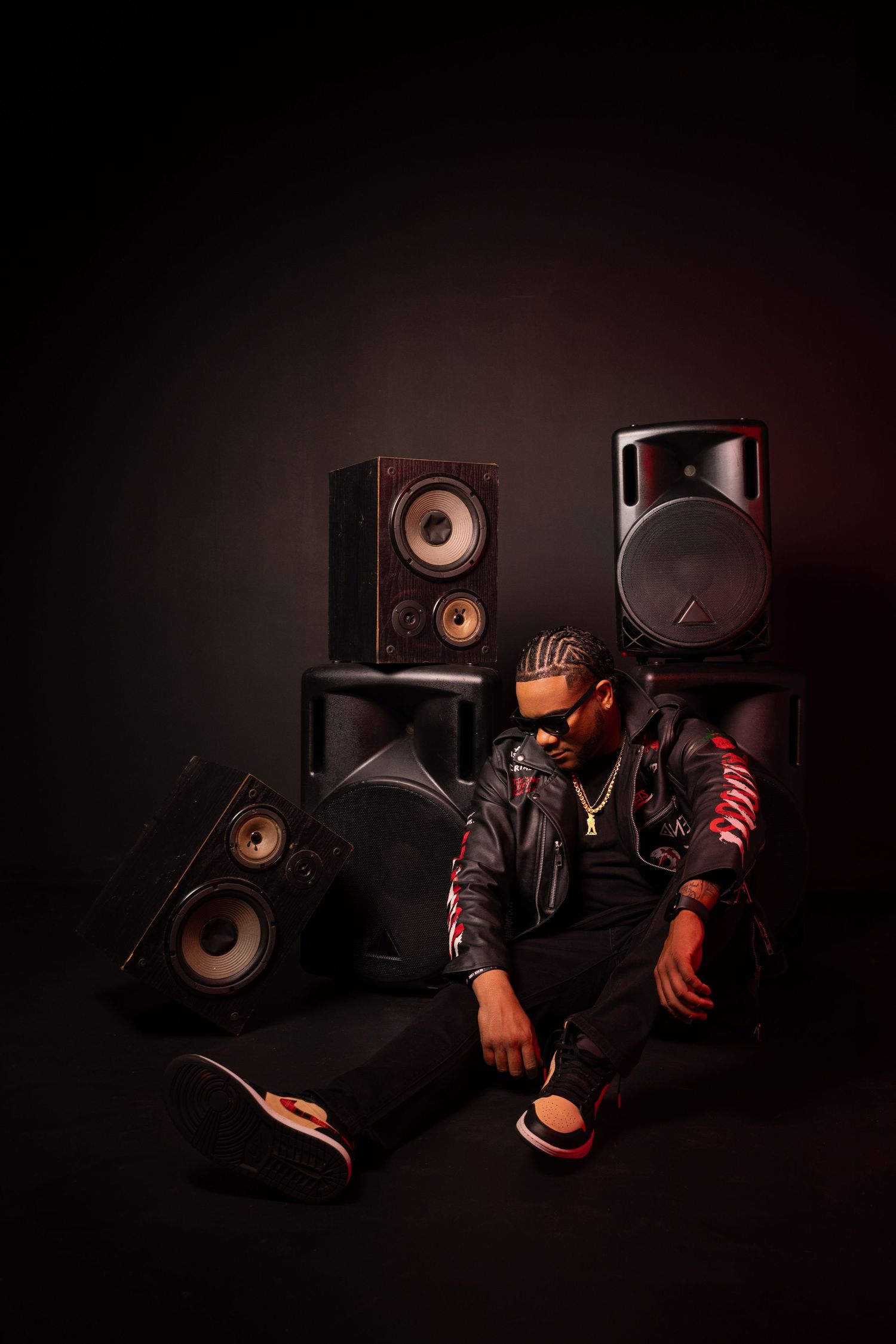 A musician poses in dark setting surrounded by professional studio speakers and monitors.